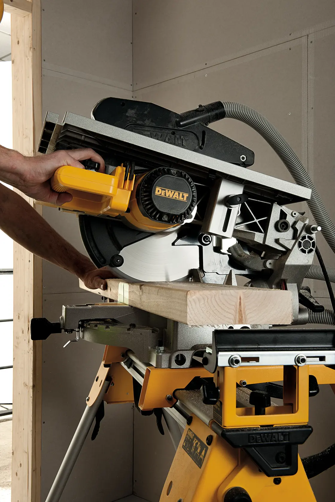 A person is using a DEWALT D27113 saw to cut a piece of wood. The saw is mounted on a yellow stand and is operating in an indoor workshop.