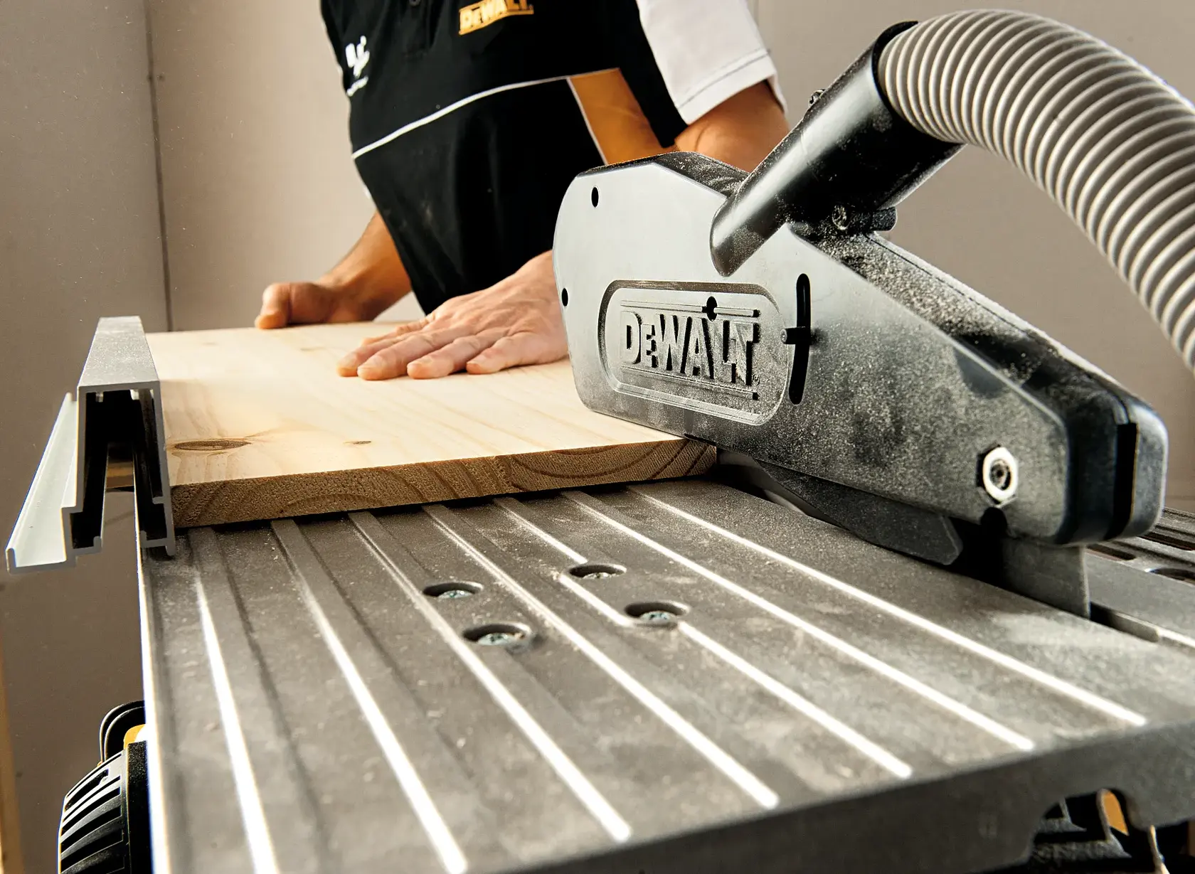 Close-up view of a DEWALT table saw in use, with a person guiding a piece of wood through the saw in a workshop environment.