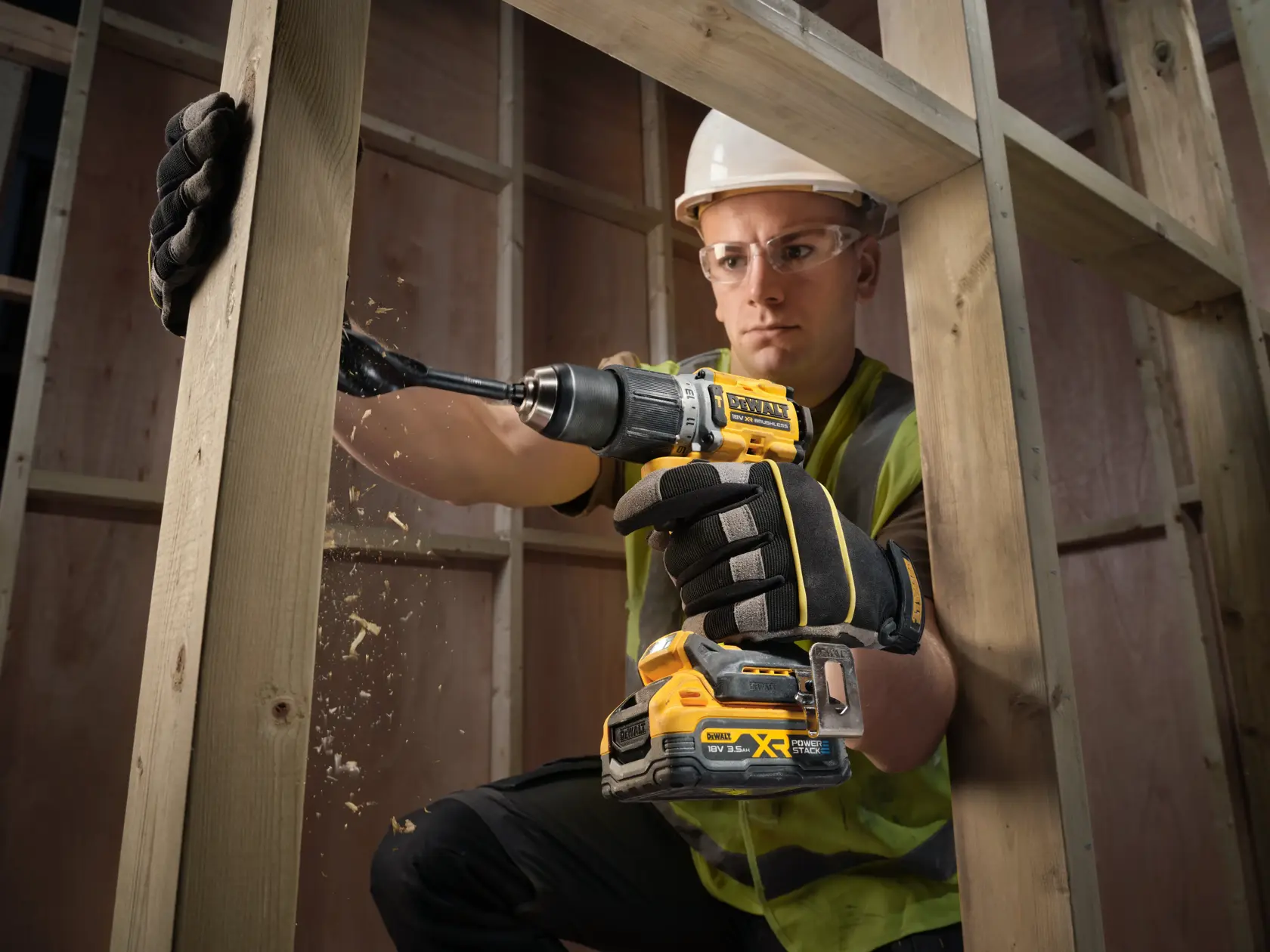 Ouvrier perce une poutre en bois avec une perceuse DEWALT sans fil, gants et équipement de sécurité.