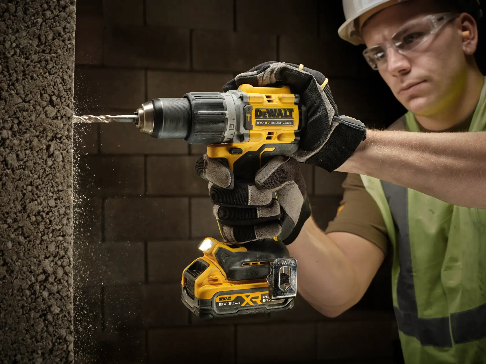 Personne gantée perce un mur en béton avec une perceuse sans fil DEWALT, poussière visible autour du foret.