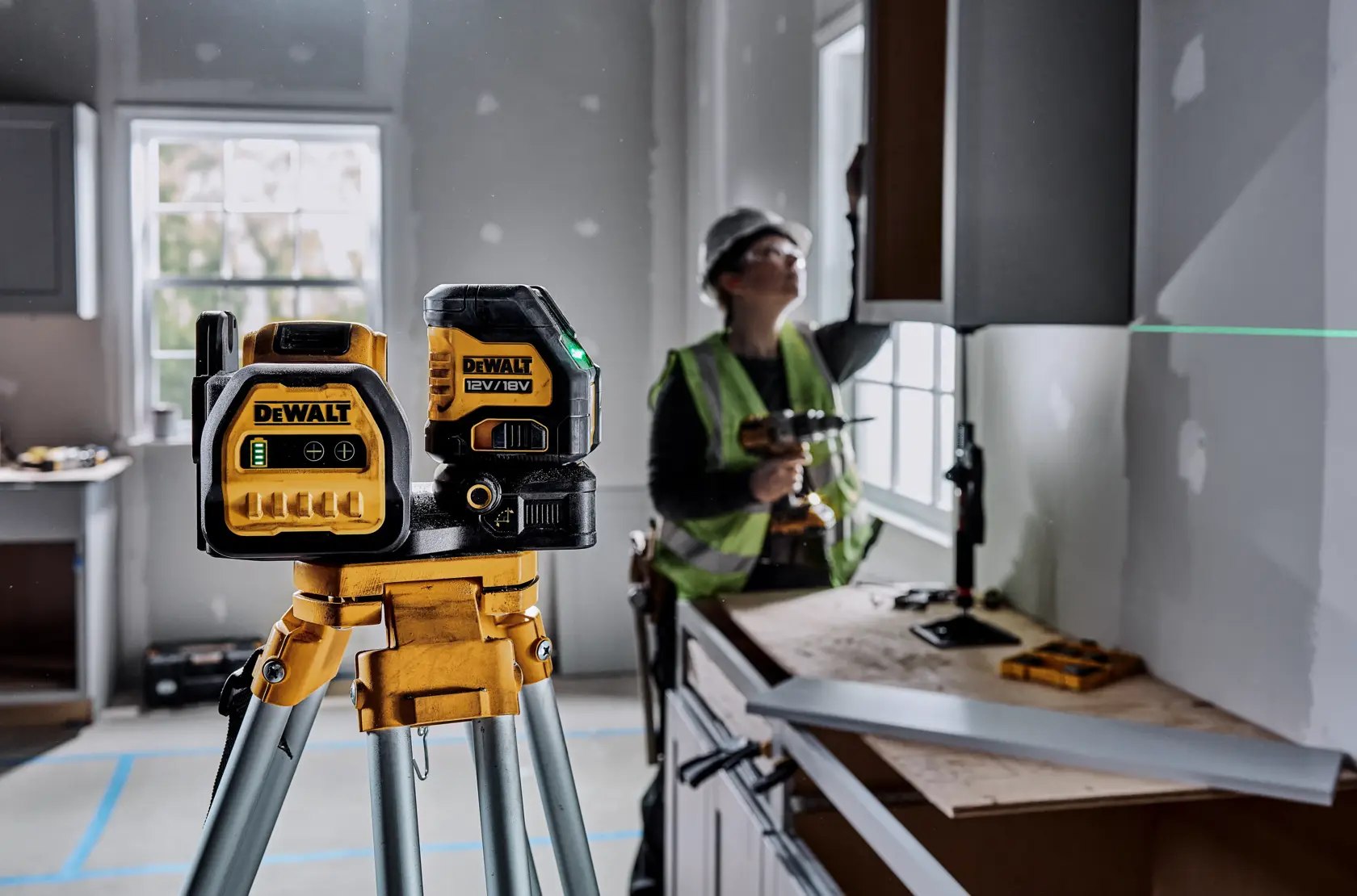 DEWALT Lasergerät (DCE088D1G18-QW, DCE088D1G18) auf Stativ, Einsatz auf Baustelle, Arbeiter im Hintergrund.