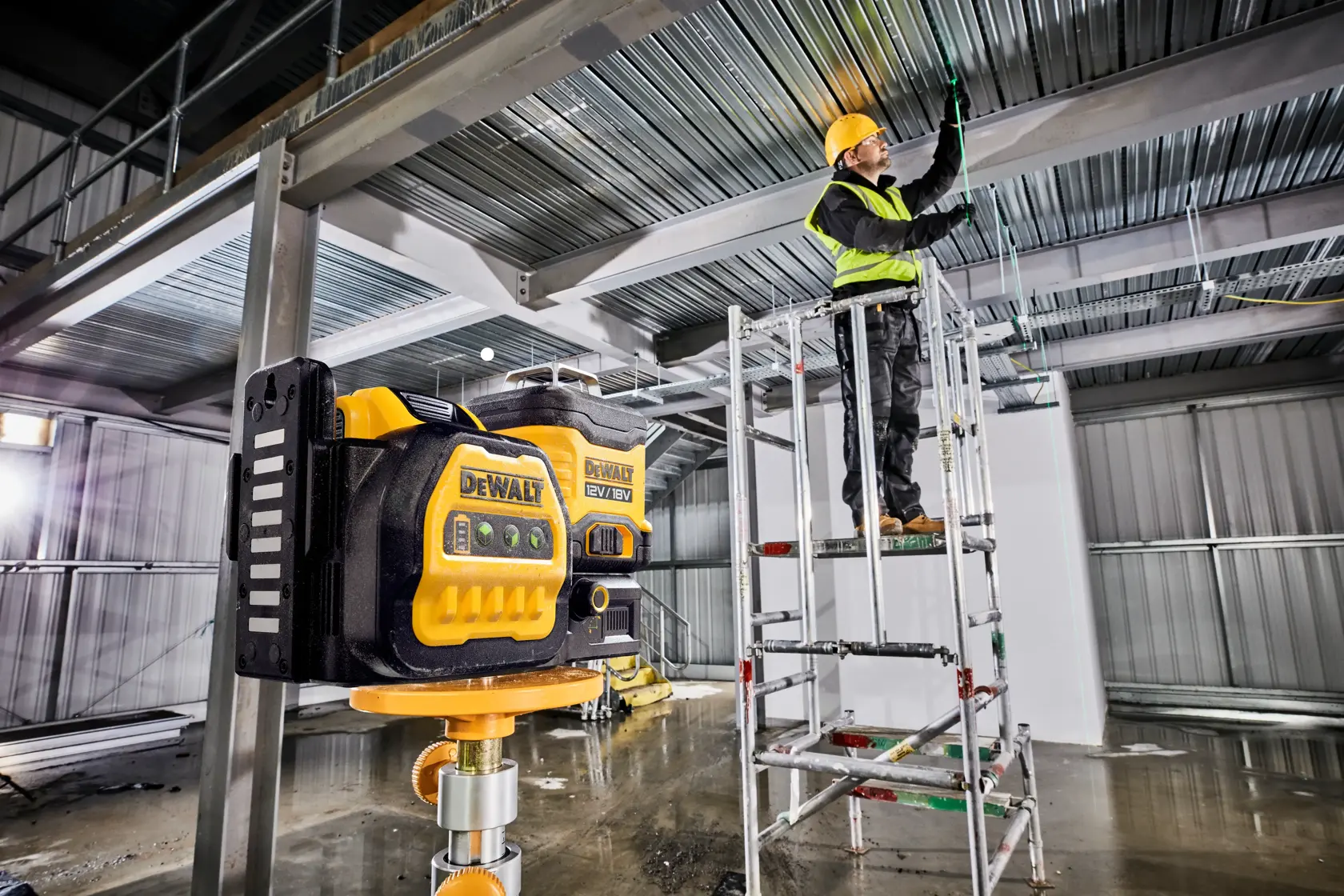 DEWALT Lasergerät am Bau, Arbeiter auf Gerüst justiert Deckenverkabelung.