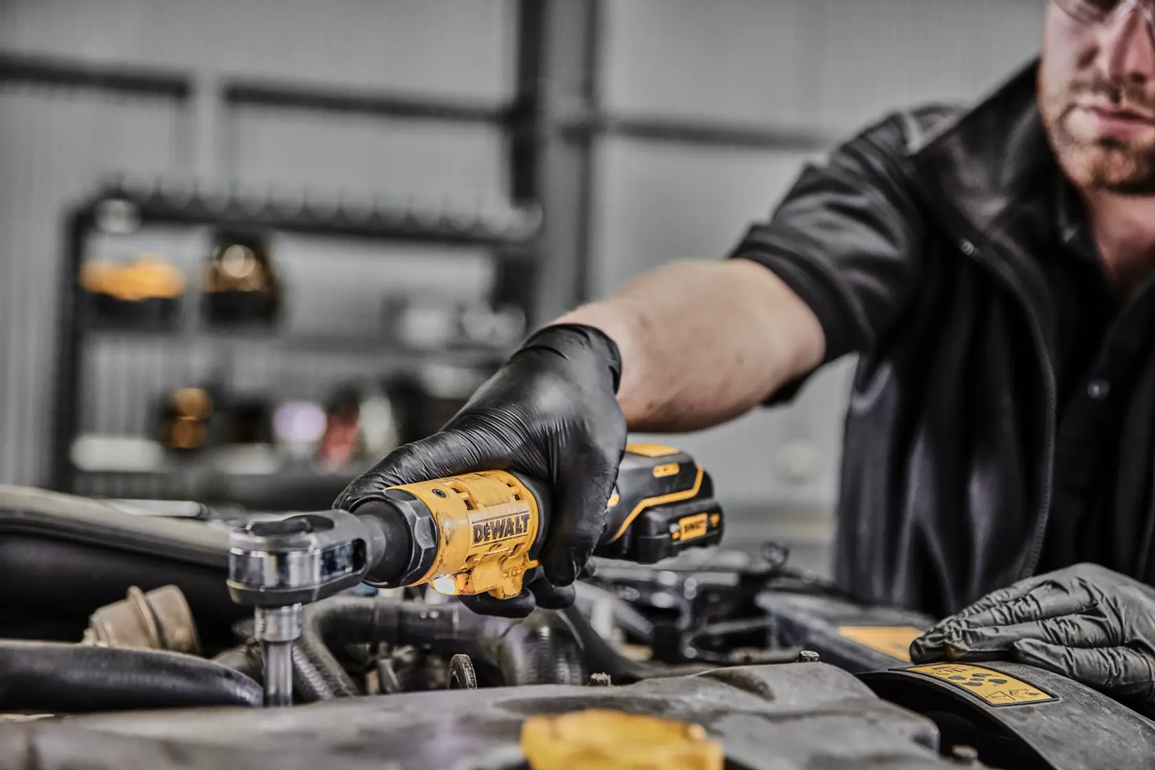 Una persona con guantes negros utiliza una herramienta de carraca inalámbrica DEWALT DCF504N para trabajar en el motor de un coche en un taller.