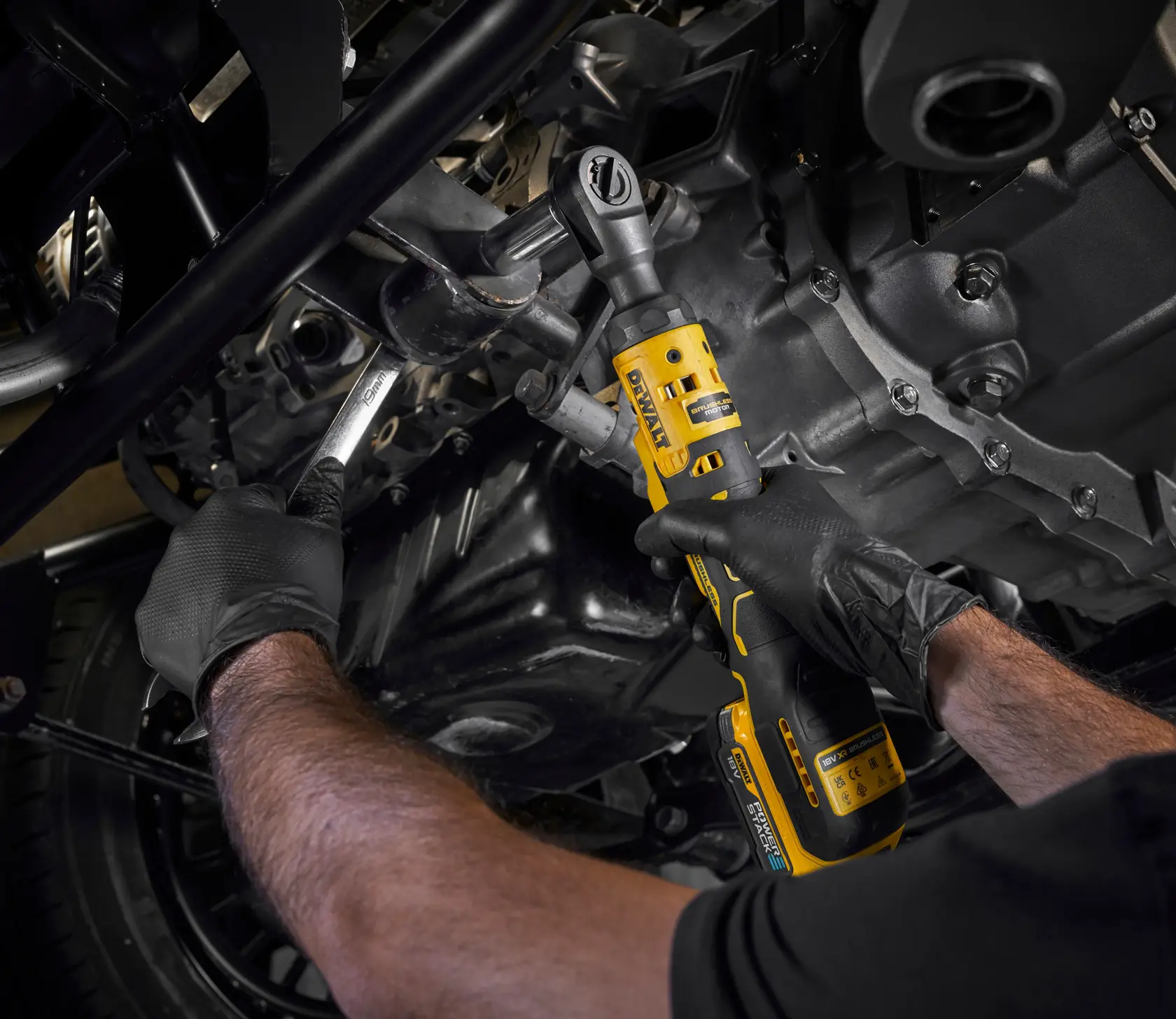 Person arbeitet mit einem DEWALT Akku-Ratschenschlüssel am Motor und trägt schwarze Handschuhe.