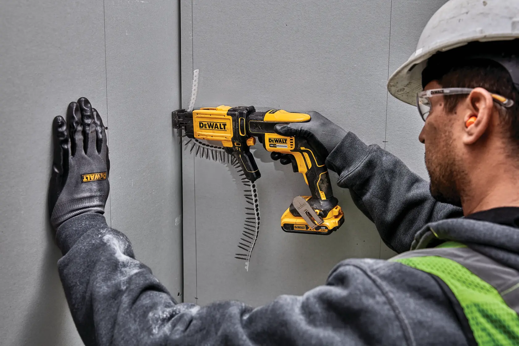 Trabajador usa la herramienta DEWALT DCF6202 para drywall, con guantes, casco y gafas protectoras.