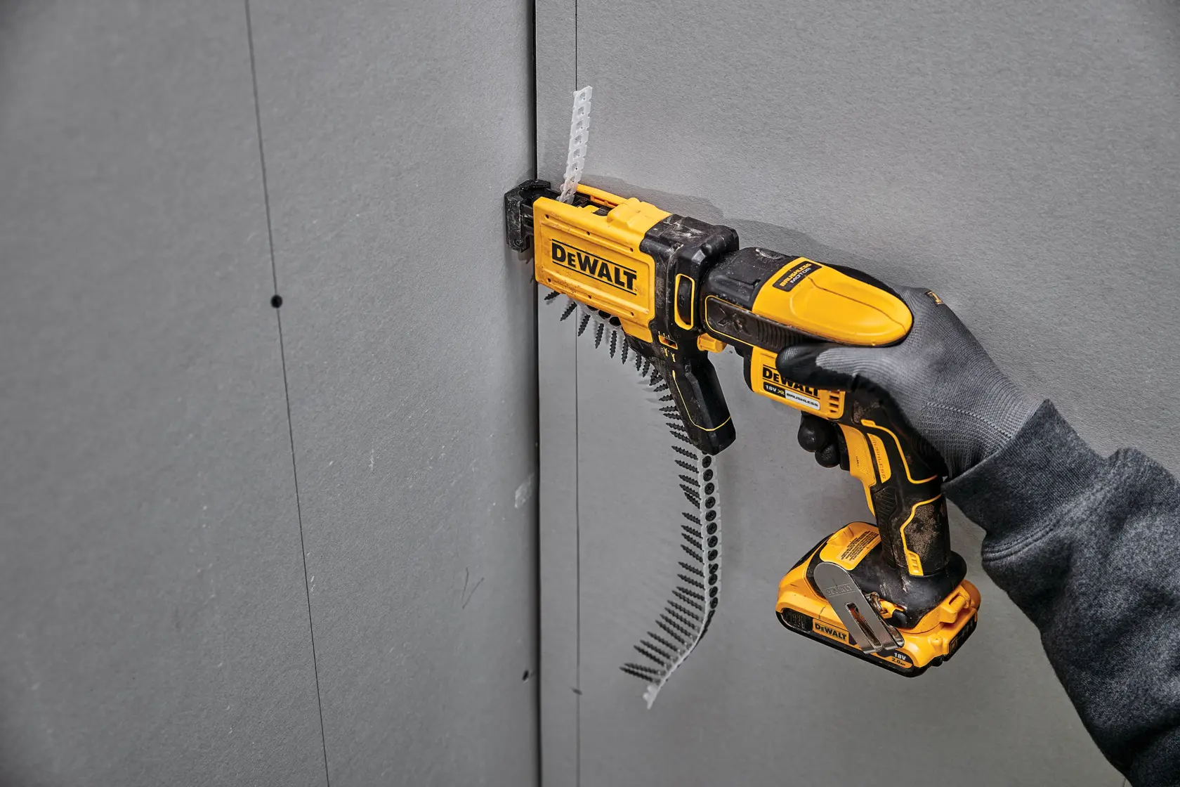 Atornilladora DEWALT DCF6202 colocando tornillos en panel de yeso, sostenida por mano enguantada.