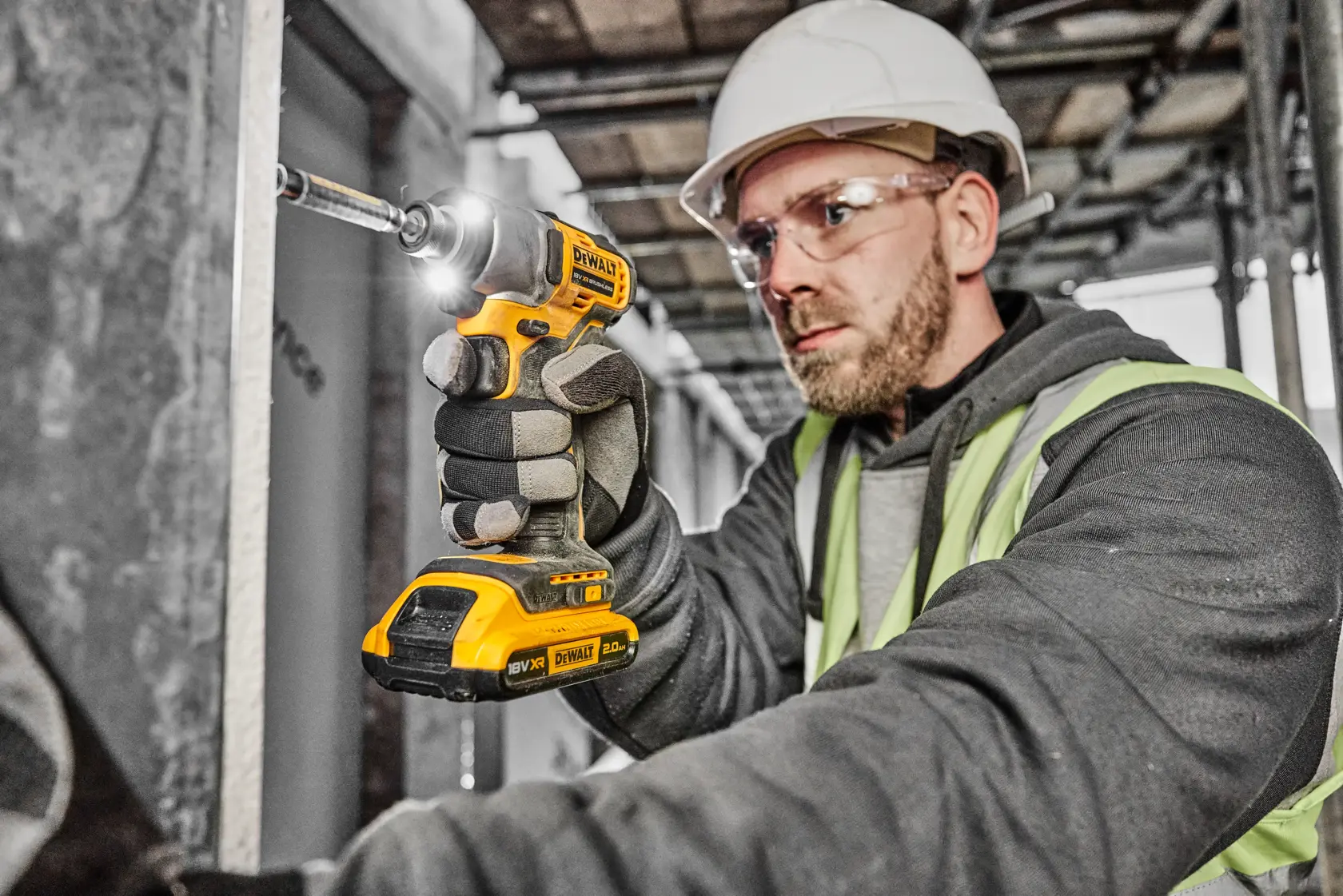 A person wearing a hard hat and safety vest is using a DEWALT cordless impact driver (model DCF840D2T) on a construction site.