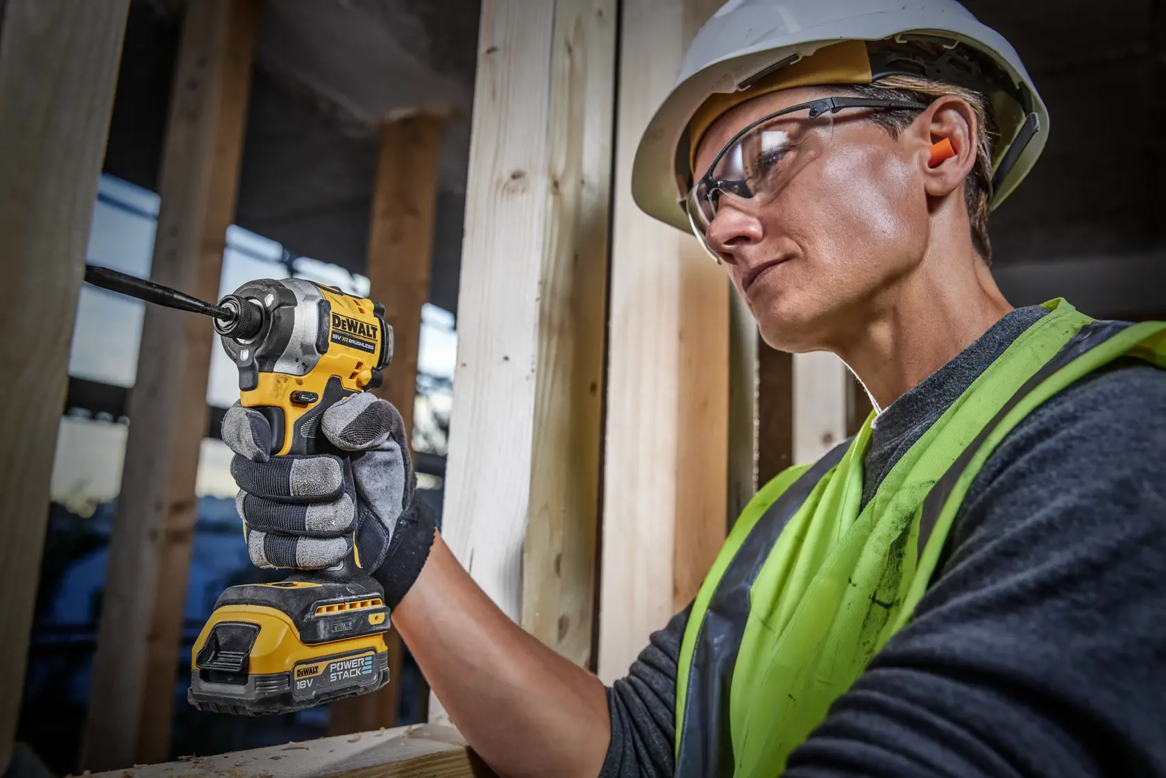 Persona con casco y chaleco de alta visibilidad utilizando una herramienta eléctrica inalámbrica DEWALT, concretamente un atornillador de impacto, en una obra de construcción.