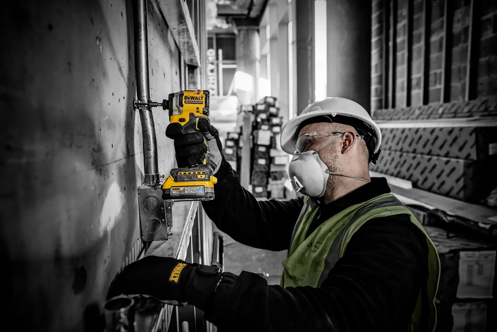 Trabajador usa DEWALT DCF850E2T en tubería, con guantes y equipo de seguridad, en obra de construcción.