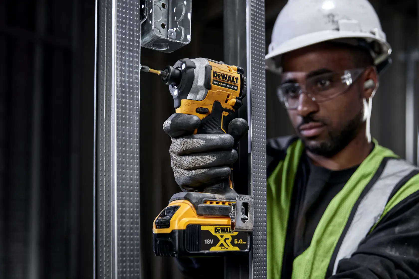 Mano enguantada usa DEWALT DCF850NT atornillador en marco metálico en obra.