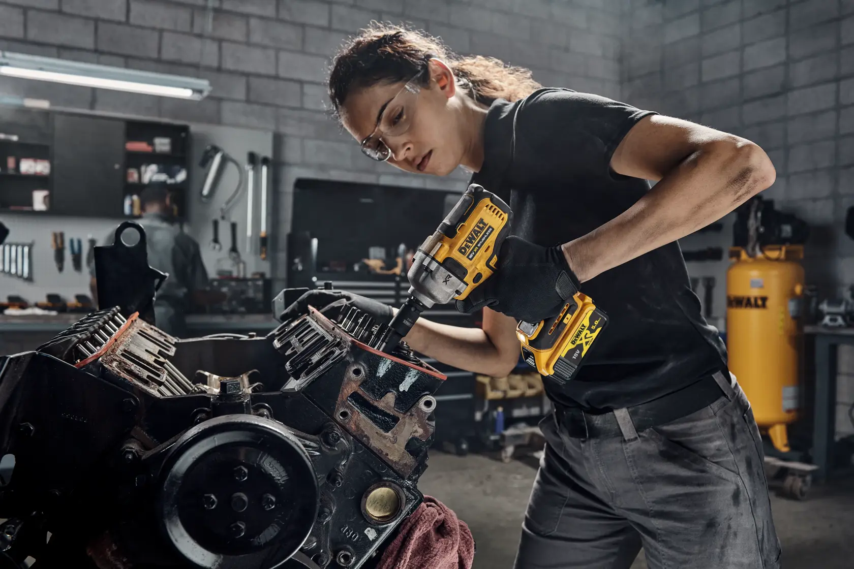 Persona utiliza una llave de impacto DEWALT DCF891P2T en una pieza de máquina en taller con herramientas detrás.