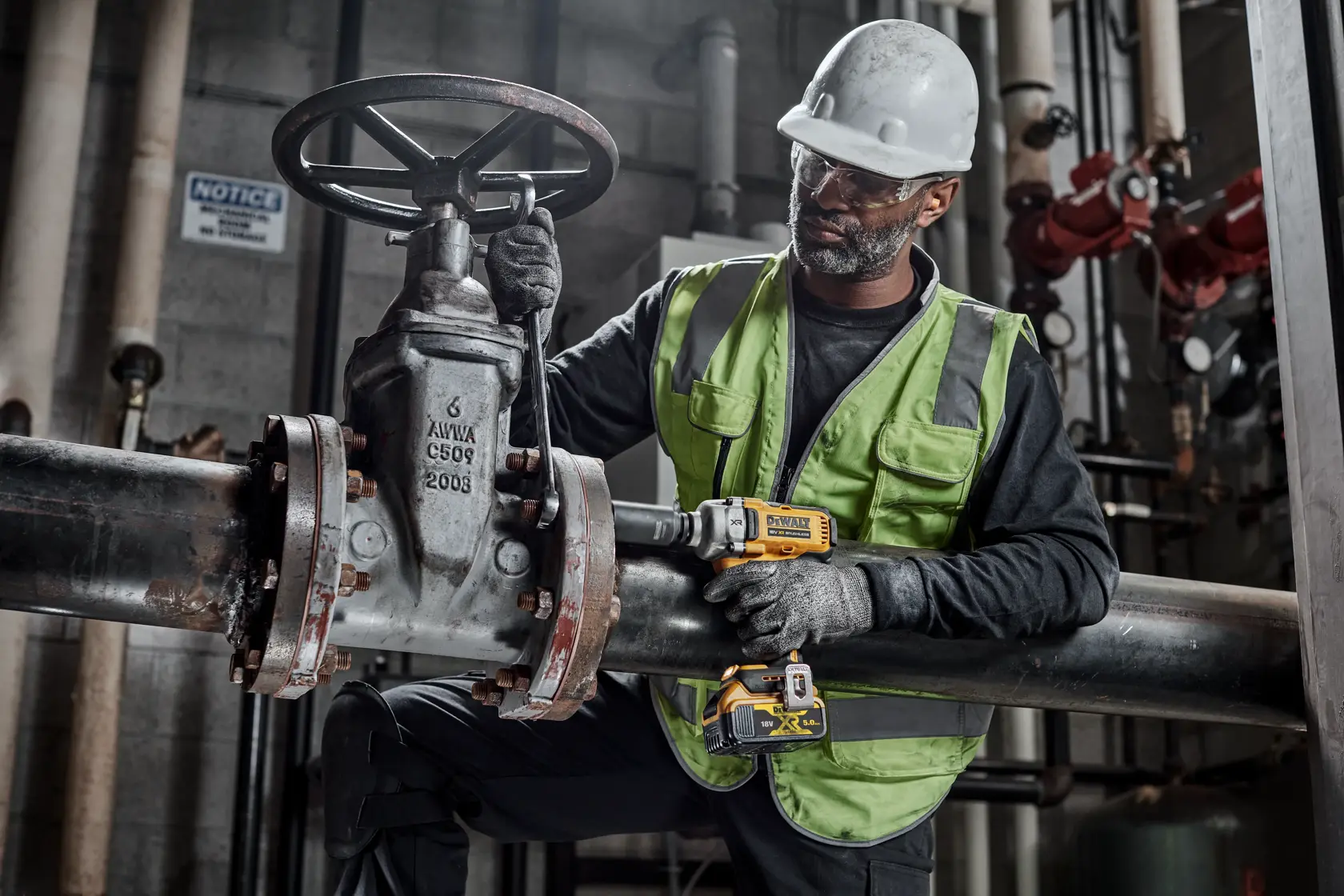 Arbeiter nutzt DEWALT DCF892NT Werkzeug an Rohr, mit Sicherheitsausrüstung und Warnweste, im Innenbereich.