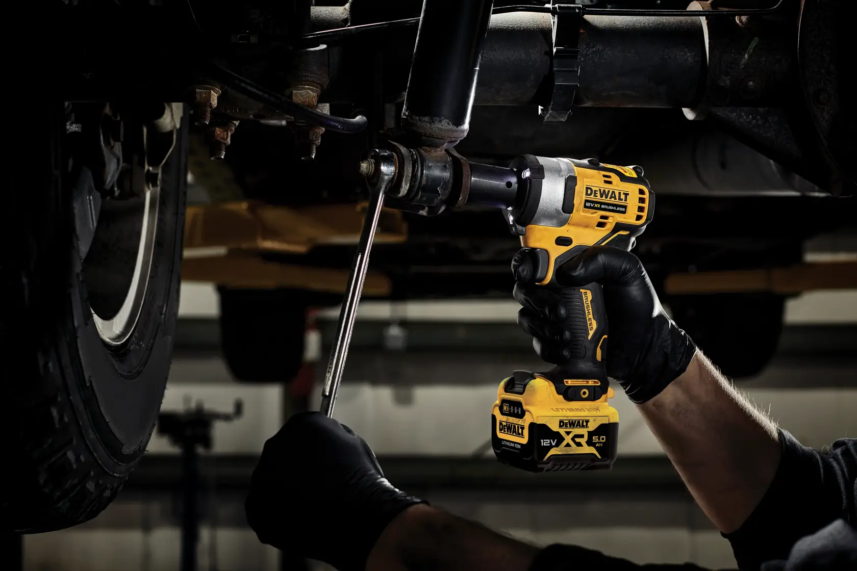 DEWALT cordless impact wrench used on car undercarriage by gloved hands in a workshop.