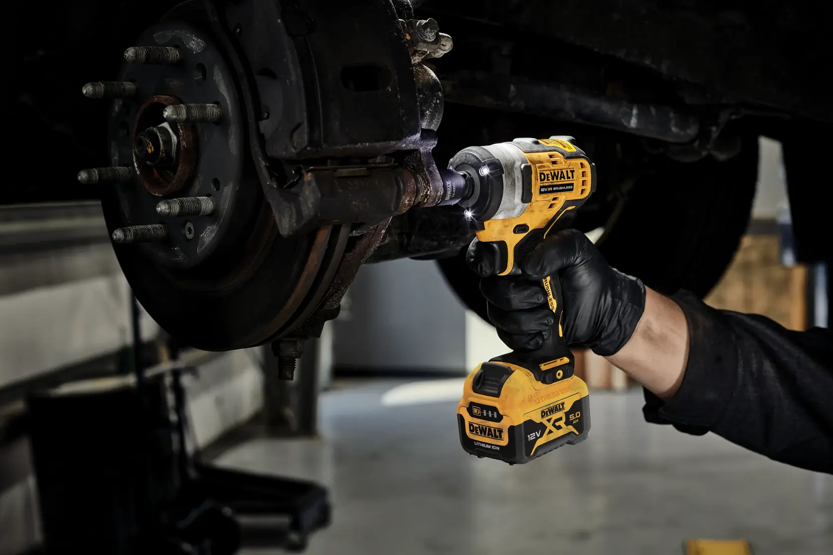 DEWALT cordless impact wrench being used on a car wheel by a gloved hand in a garage setting.