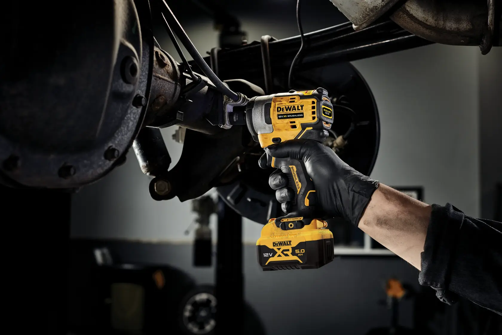 Person uses DEWALT DCF901P1 impact wrench on vehicle part in workshop.
