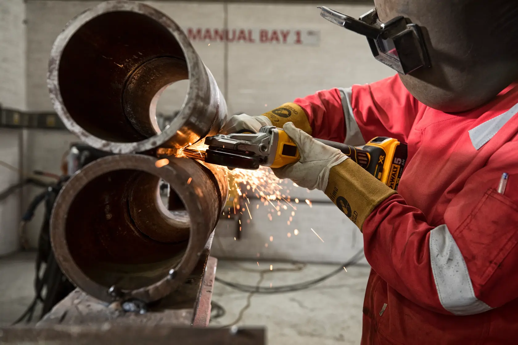 Trabajador usa amoladora inalámbrica DEWALT con chispas en tubos metálicos en taller industrial.