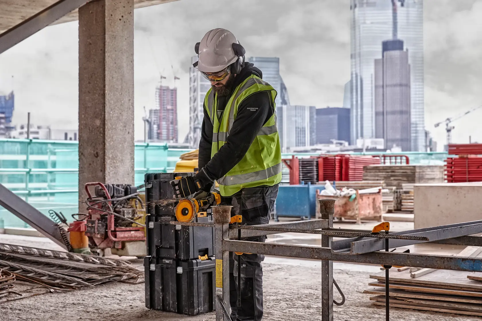 Trabajador usa herramienta DEWALT DCG418NT en obra, con equipo de seguridad y edificios urbanos de fondo.