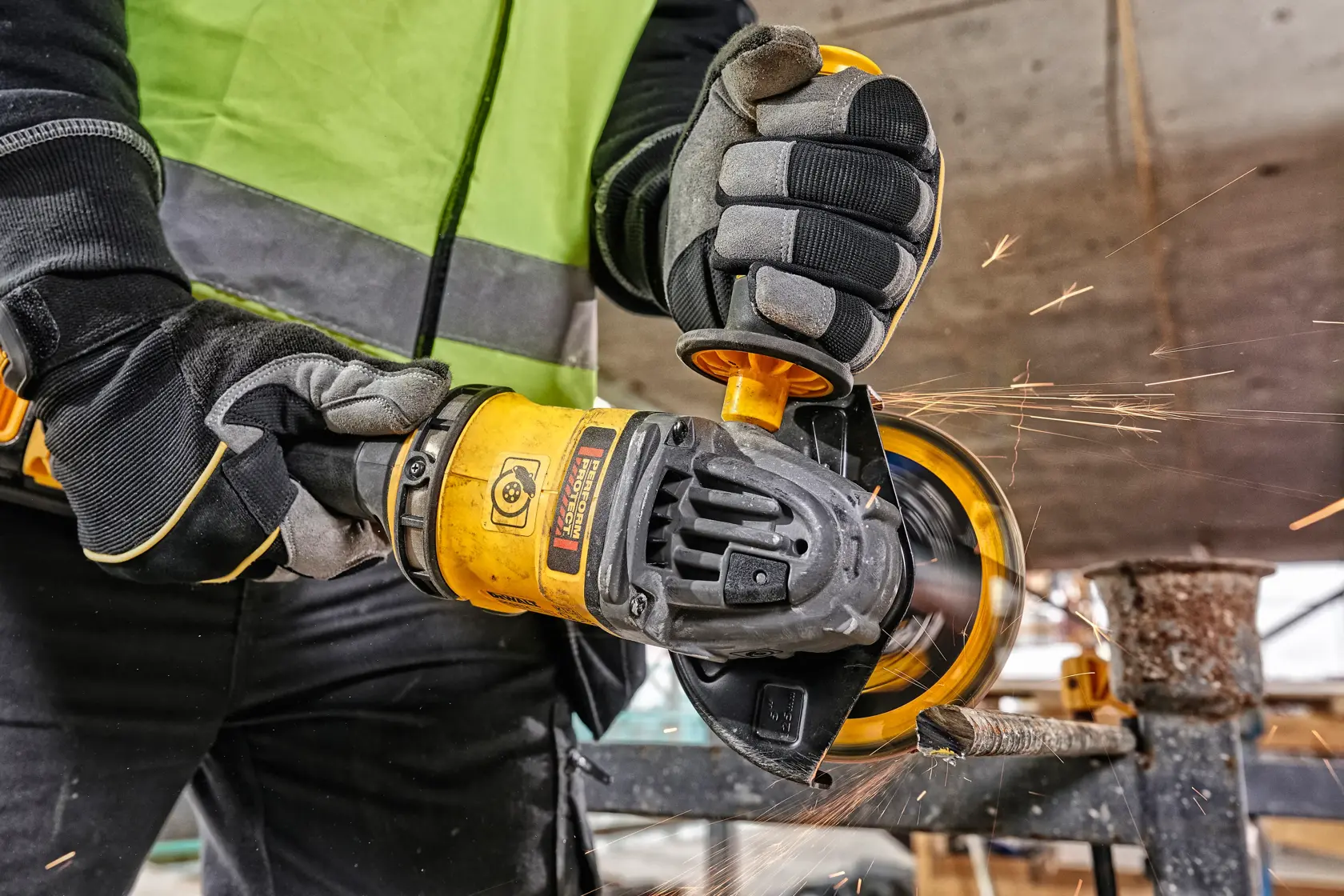 Trabajador usa amoladora DEWALT con chispas al cortar metal en un sitio de construcción.