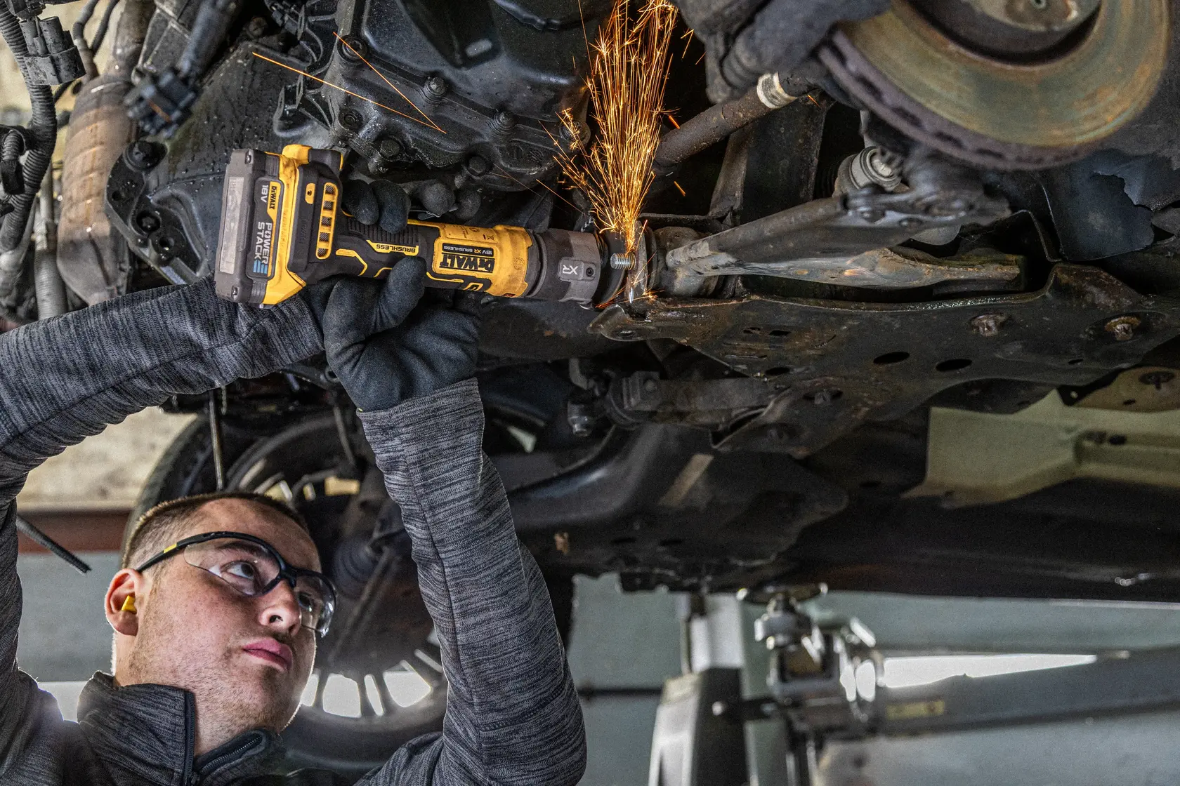 Person using DEWALT angle grinder under a car, cutting metal with sparks flying.