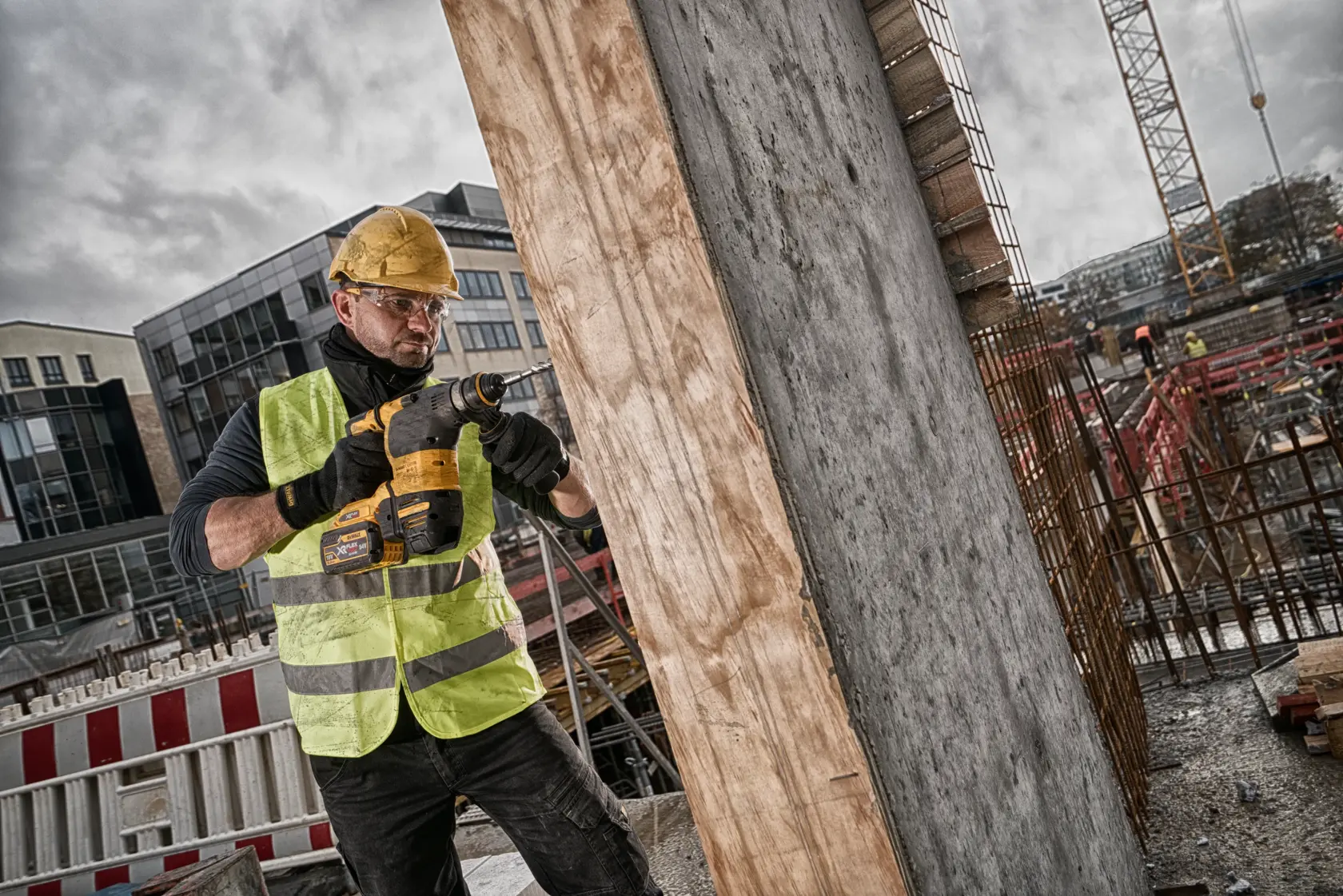 Trabajador perfora concreto en una obra con herramienta DEWALT, llevando casco y chaleco de seguridad.