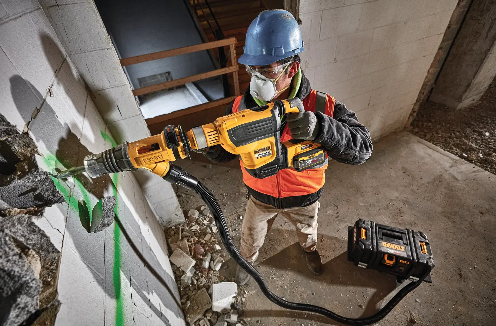 Trabajador usa herramienta DEWALT para romper pared de concreto, con casco y protección.