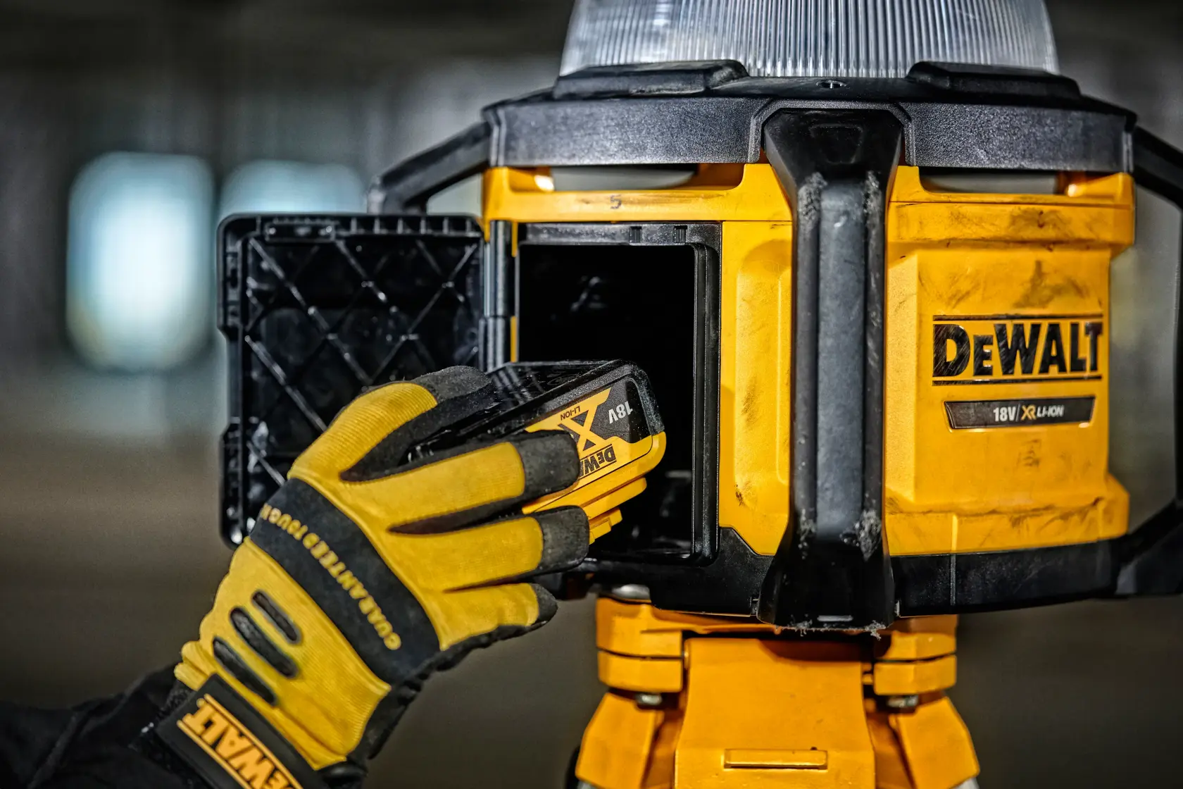 Mano enguantada inserta batería en lámpara DEWALT amarilla. Primer plano del compartimento y herramienta.