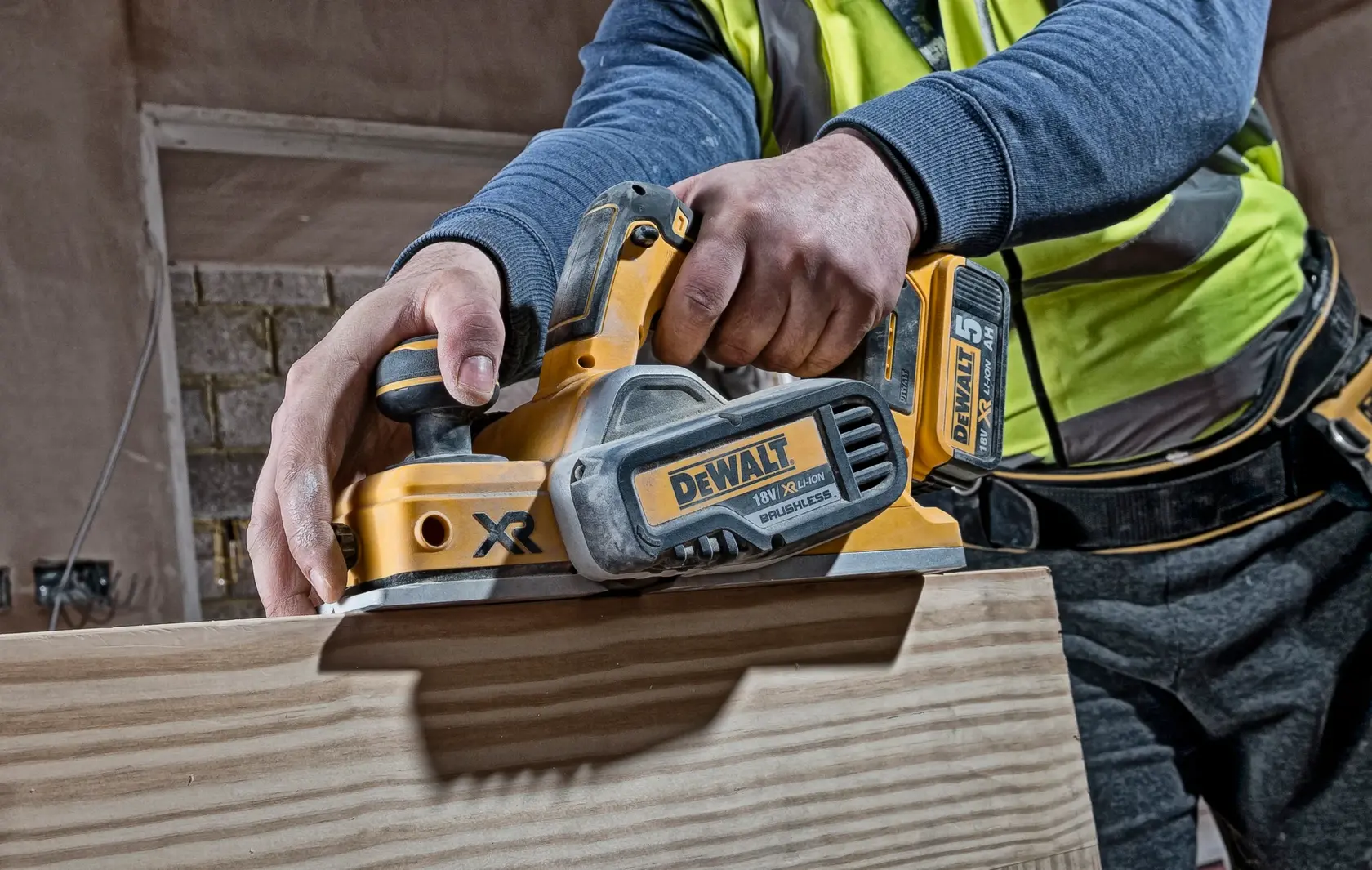 Photo of DEWALT DCP580N cordless planer in use on wood, close-up view of tool and user's hands.