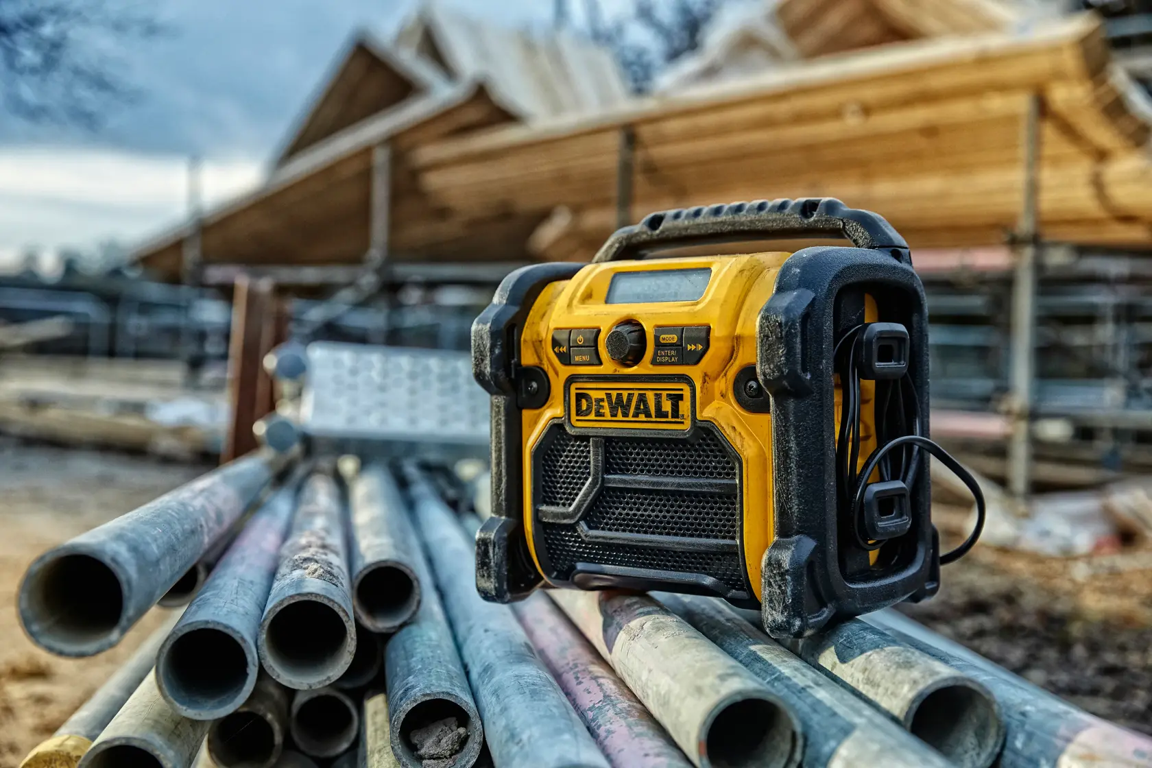 DEWALT DCR020 radio on metal pipes at a construction site, wooden structure visible in the background.
