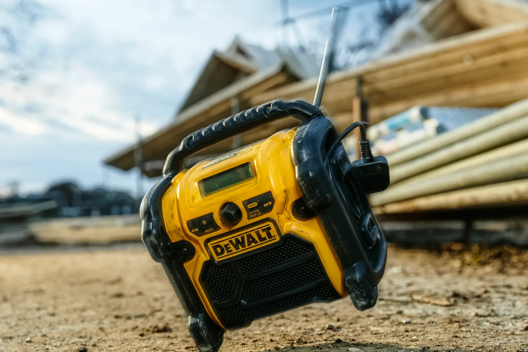 DEWALT DCR020 radio positioned outdoors on a construction site, with building materials in the background.