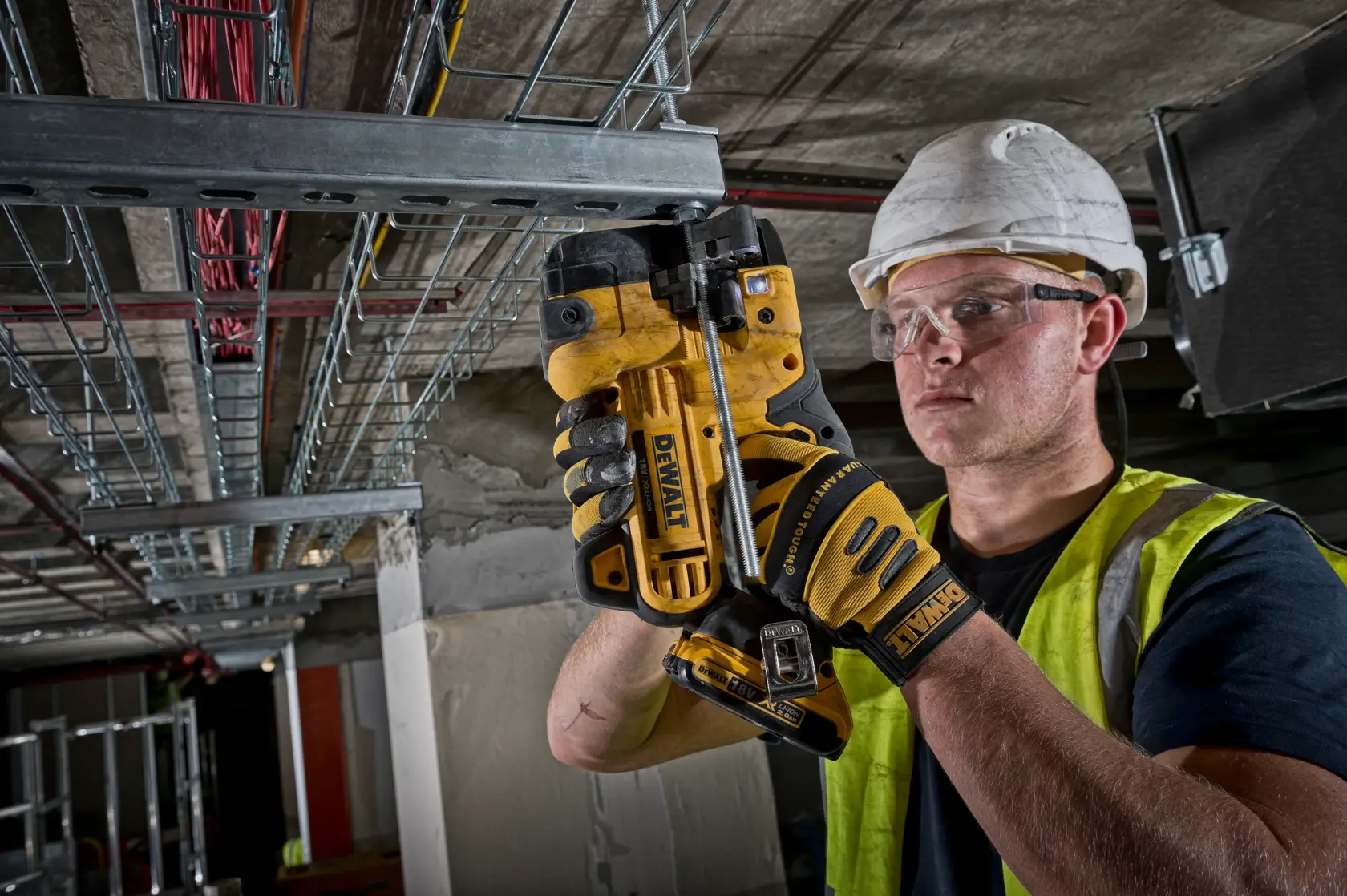 Worker using a DEWALT DCS350NT tool to cut metal conduit in an industrial setting, wearing gloves and safety gear.