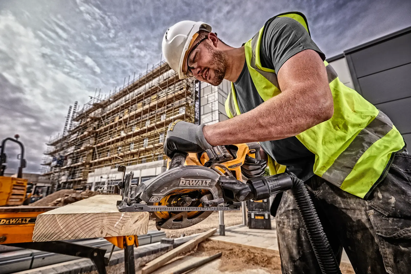 Worker uses DEWALT circular saw DCS577N to cut wood at a construction site, wearing safety gear and gloves.