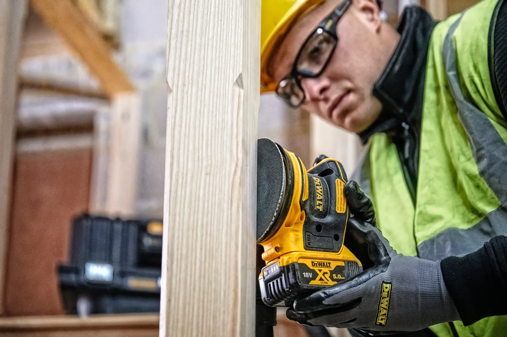 DEWALT DCW210, DCW210D1, DCW210N-XJ sander in use by worker sanding wood, construction site.