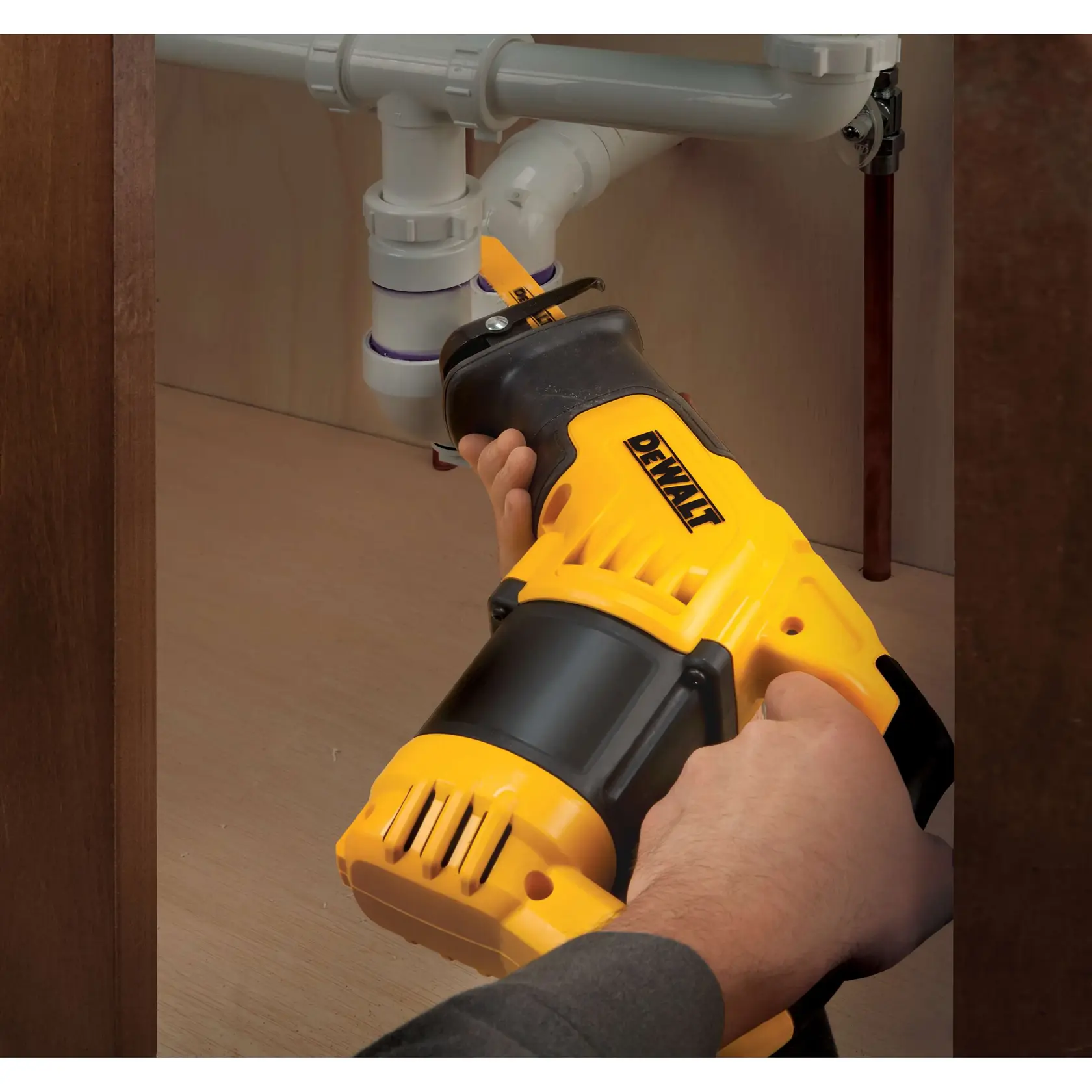 Persona usa una sierra recíproca DEWALT para cortar tubos bajo un fregadero en un gabinete.