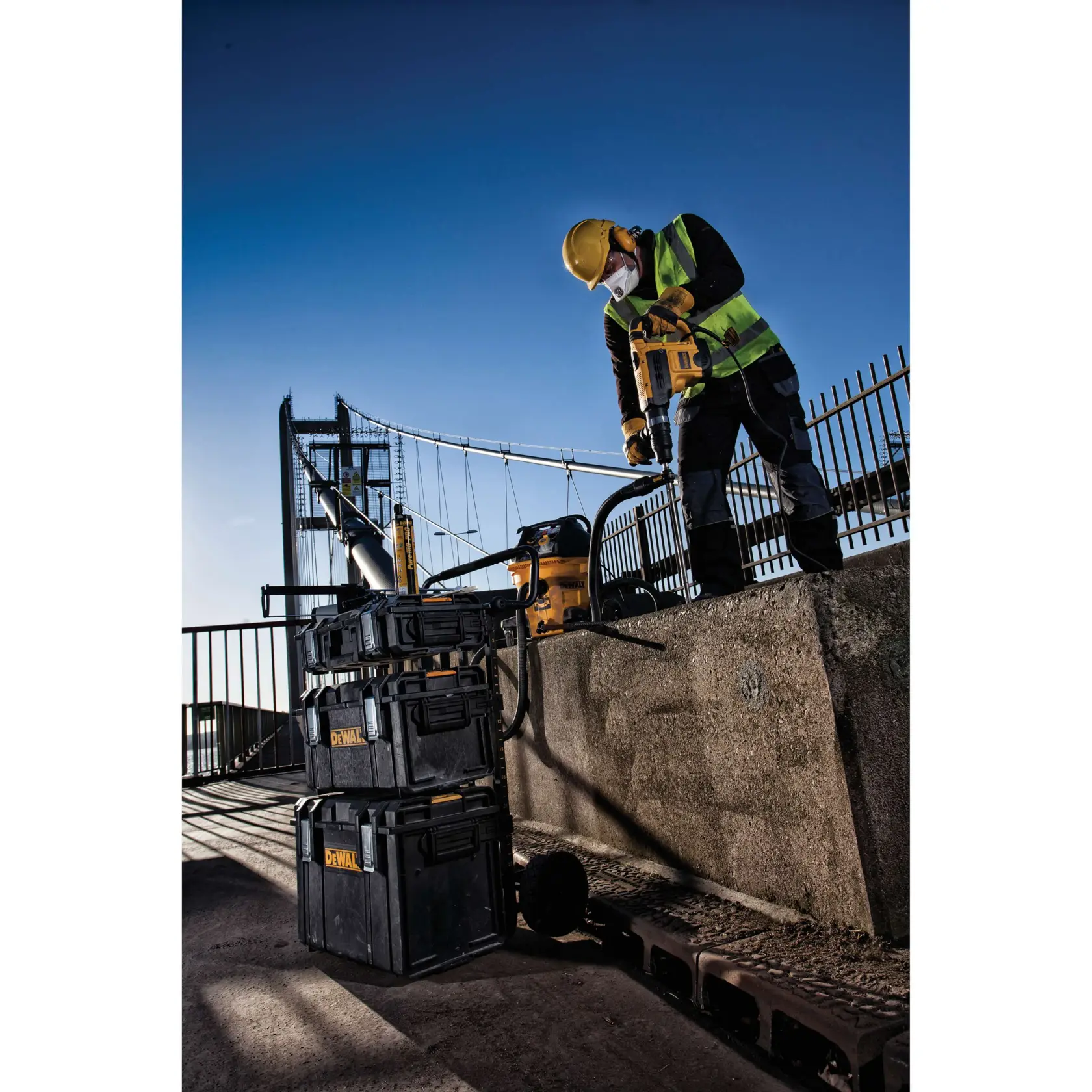 Trabajador usa herramientas y cajas DEWALT en un puente, lleva equipo de seguridad.