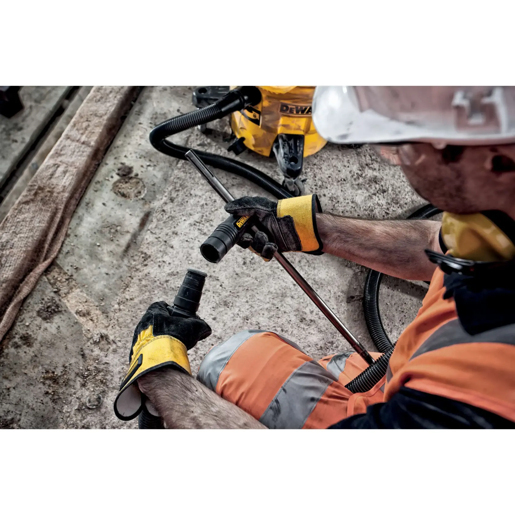 Trabajador con protección conecta manguera de aspirador DEWALT en obra con suelo de concreto.
