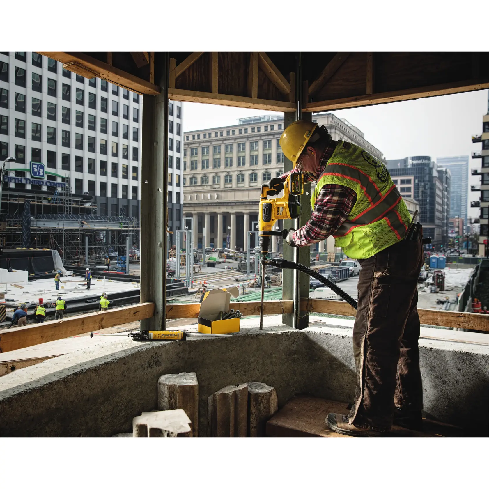 Trabajador usando taladro DEWALT DT60231 en obra, con equipo de seguridad y edificios urbanos al fondo.