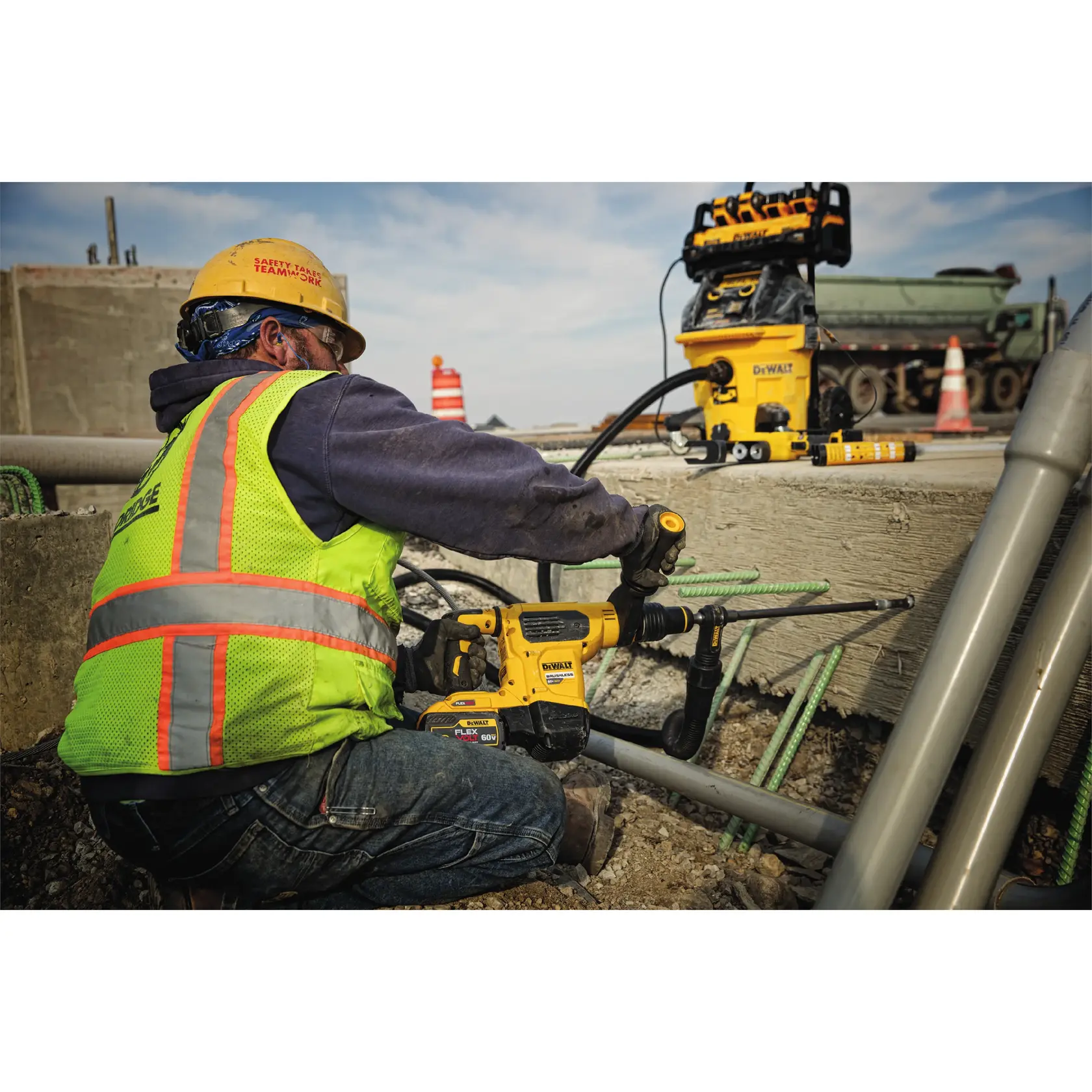 Trabajador con equipo de seguridad usa un taladro DEWALT en concreto, herramientas y tubos cercanos.