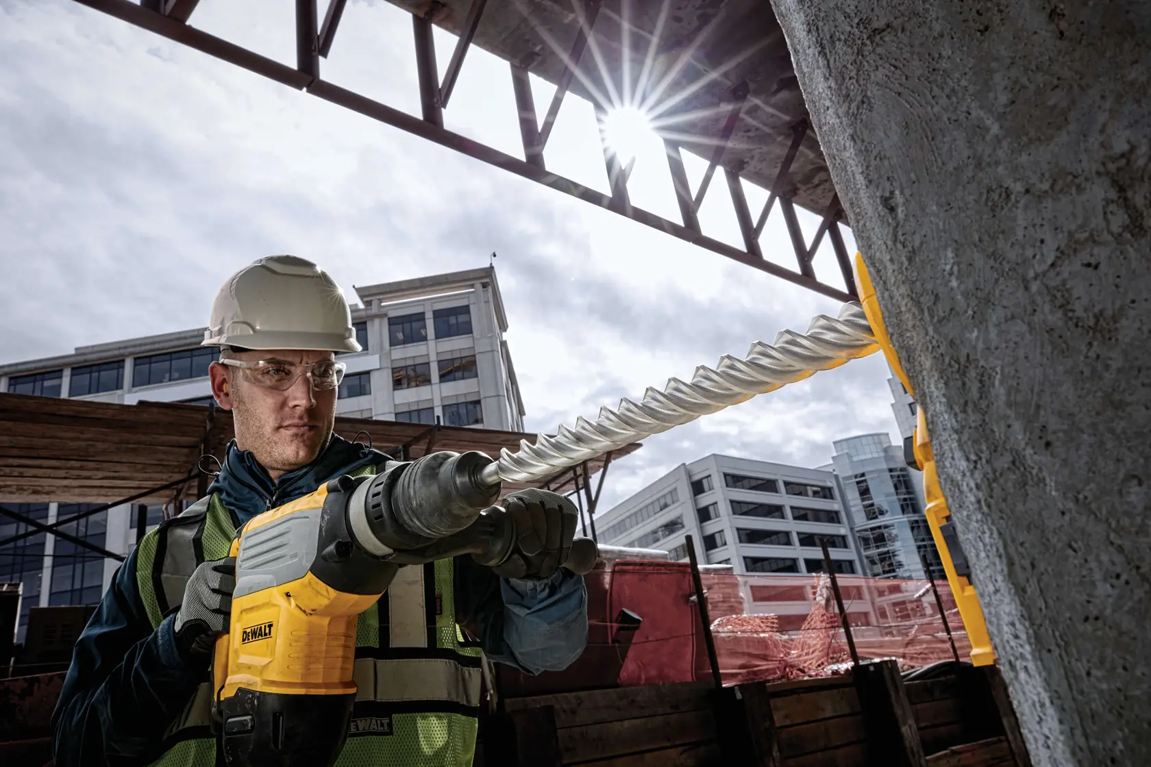 DEWALT Hammerbohrer bohrt Beton auf Baustelle, Arbeiter mit Schutzkleidung, städtischer Hintergrund.