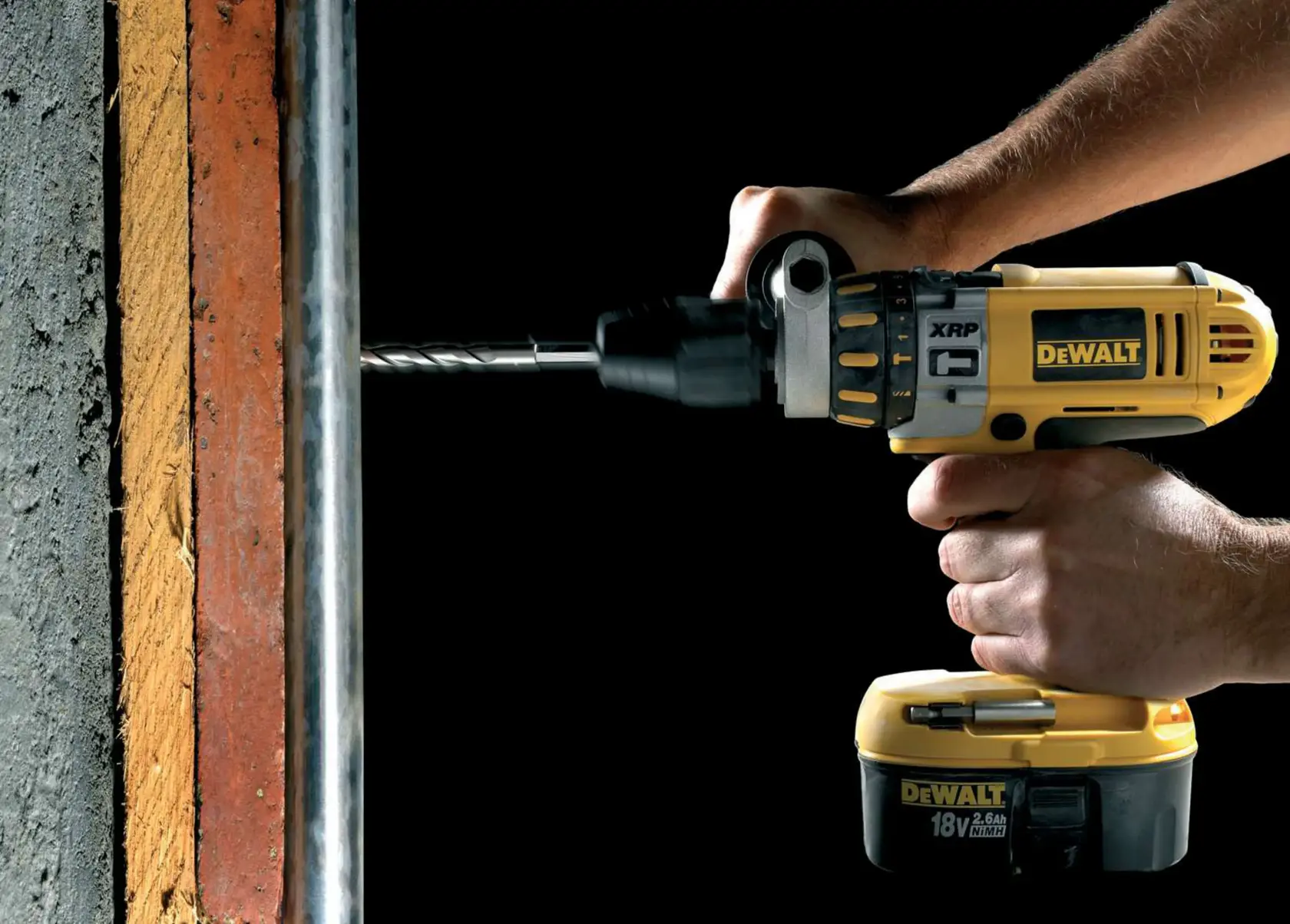 DEWALT cordless drill in use, drilling into a concrete wall. Hands grip the yellow power tool firmly.