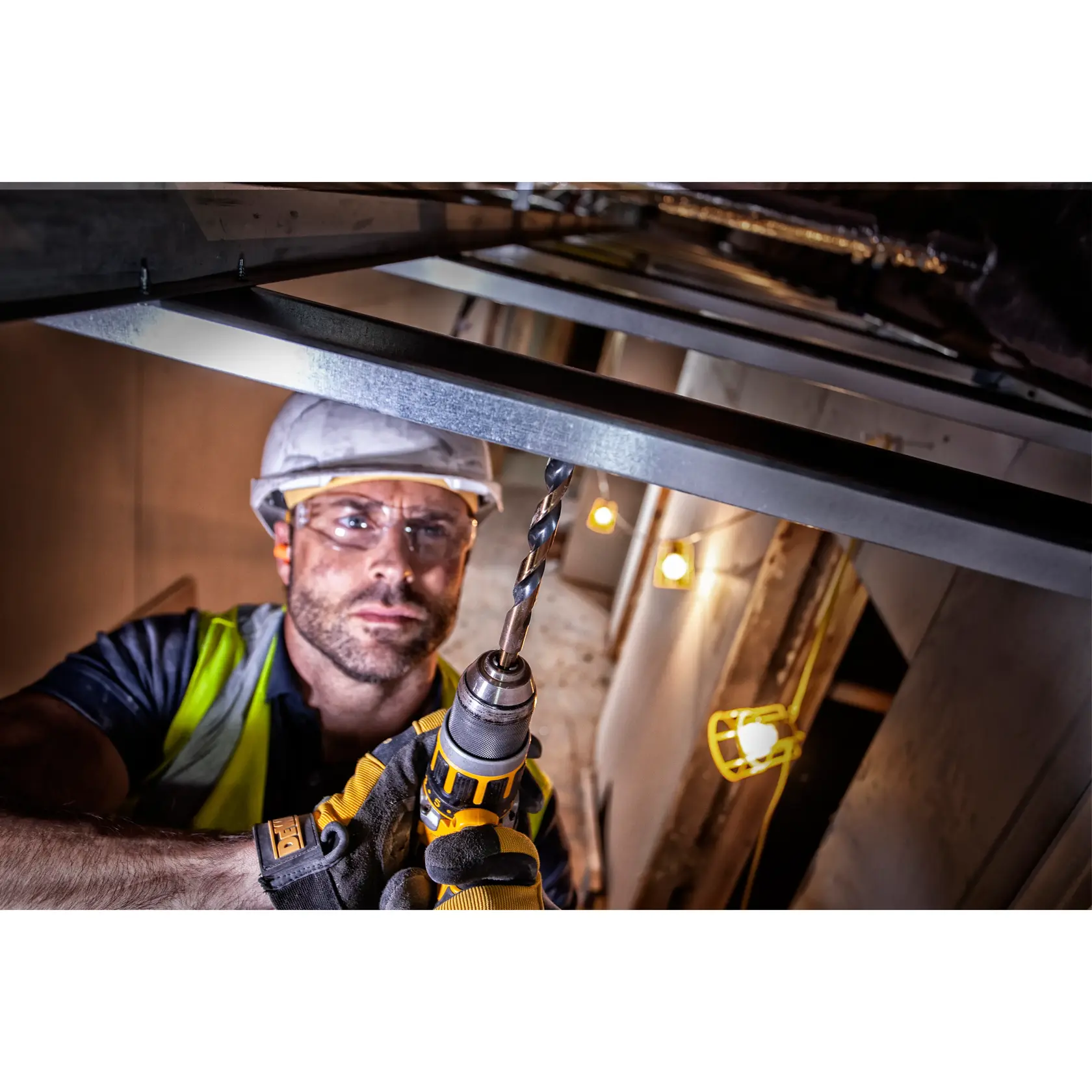 Arbeiter nutzt DEWALT-Bohrer auf Metall an Baustelle, trägt Handschuhe und Sicherheitsausrüstung.