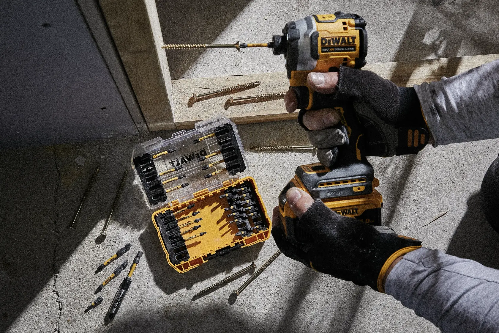 DEWALT-Bohrer schraubt in Metallrahmen auf Betonboden, Nahaufnahme von Werkzeug und Bit.