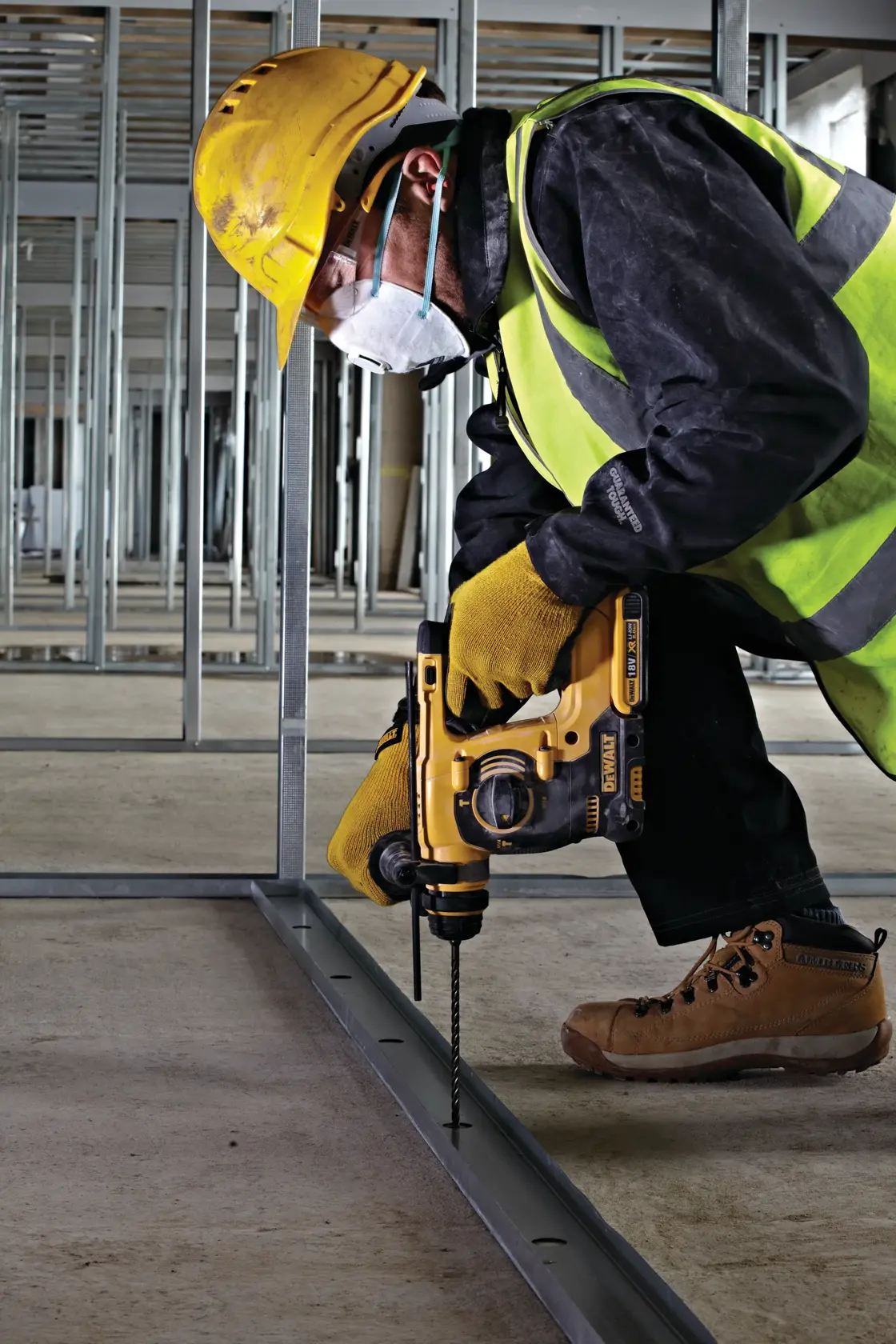 Trabajador perfora marco metálico con taladro DEWALT y equipo de seguridad en la construcción.