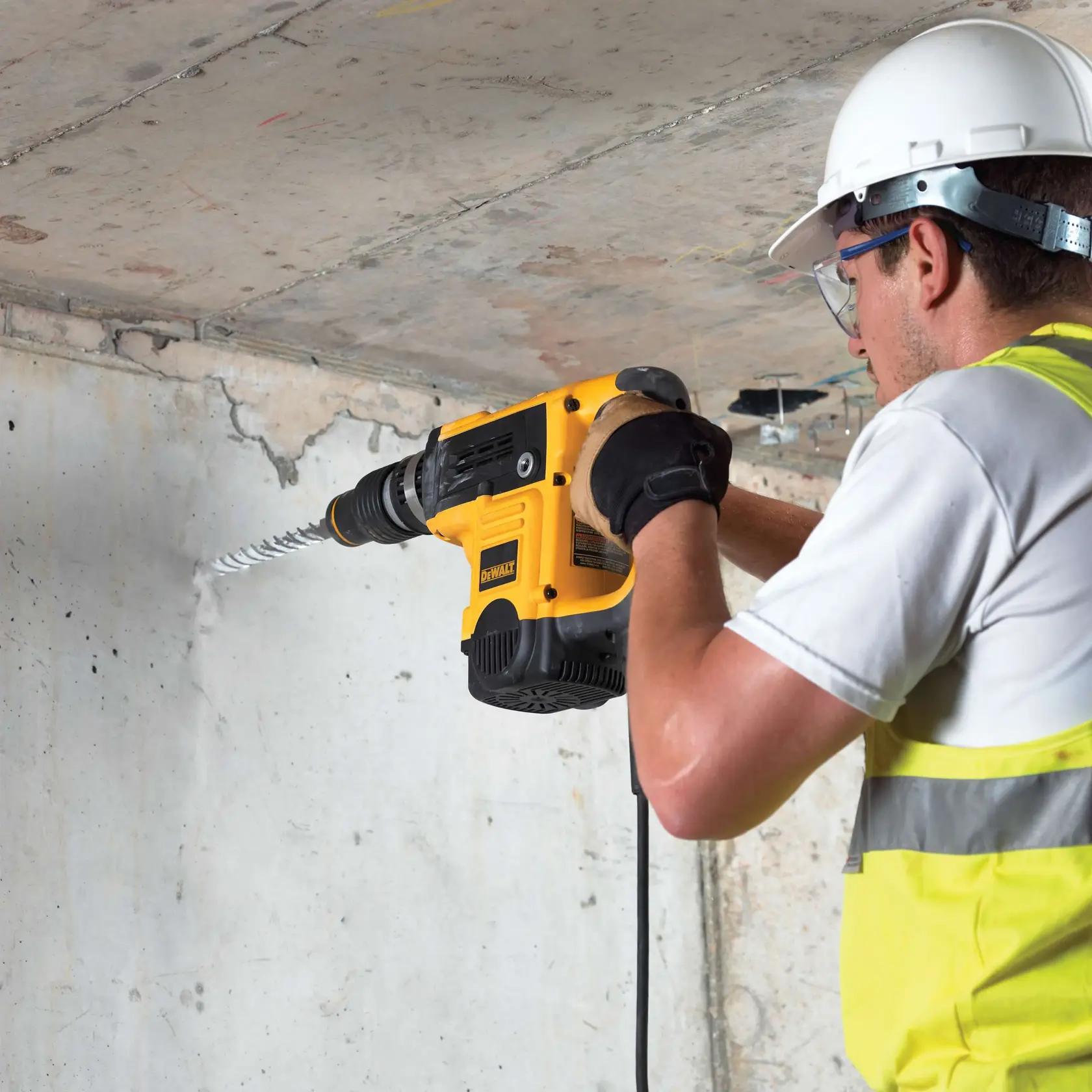 Worker uses DEWALT hammer drill with DT9424 bit to drill into concrete wall, wearing safety gear.
