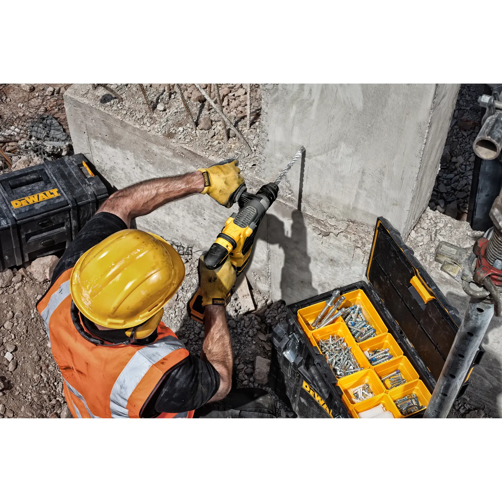 Trabajador usa taladro DEWALT en pared de concreto, caja de herramientas y sujetadores en obra.