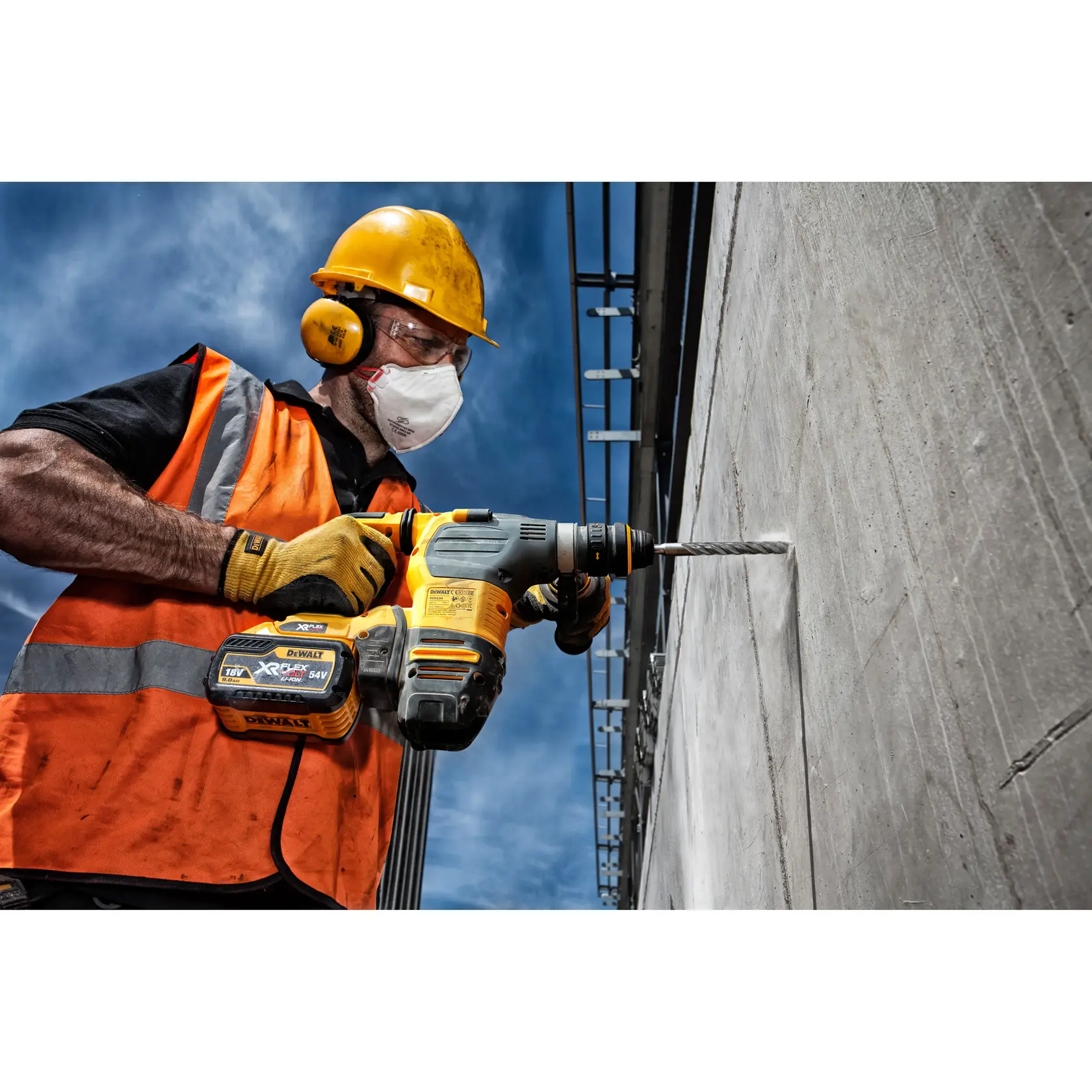 Trabajador perfora pared de hormigón con taladro DEWALT inalámbrico y equipo de seguridad.