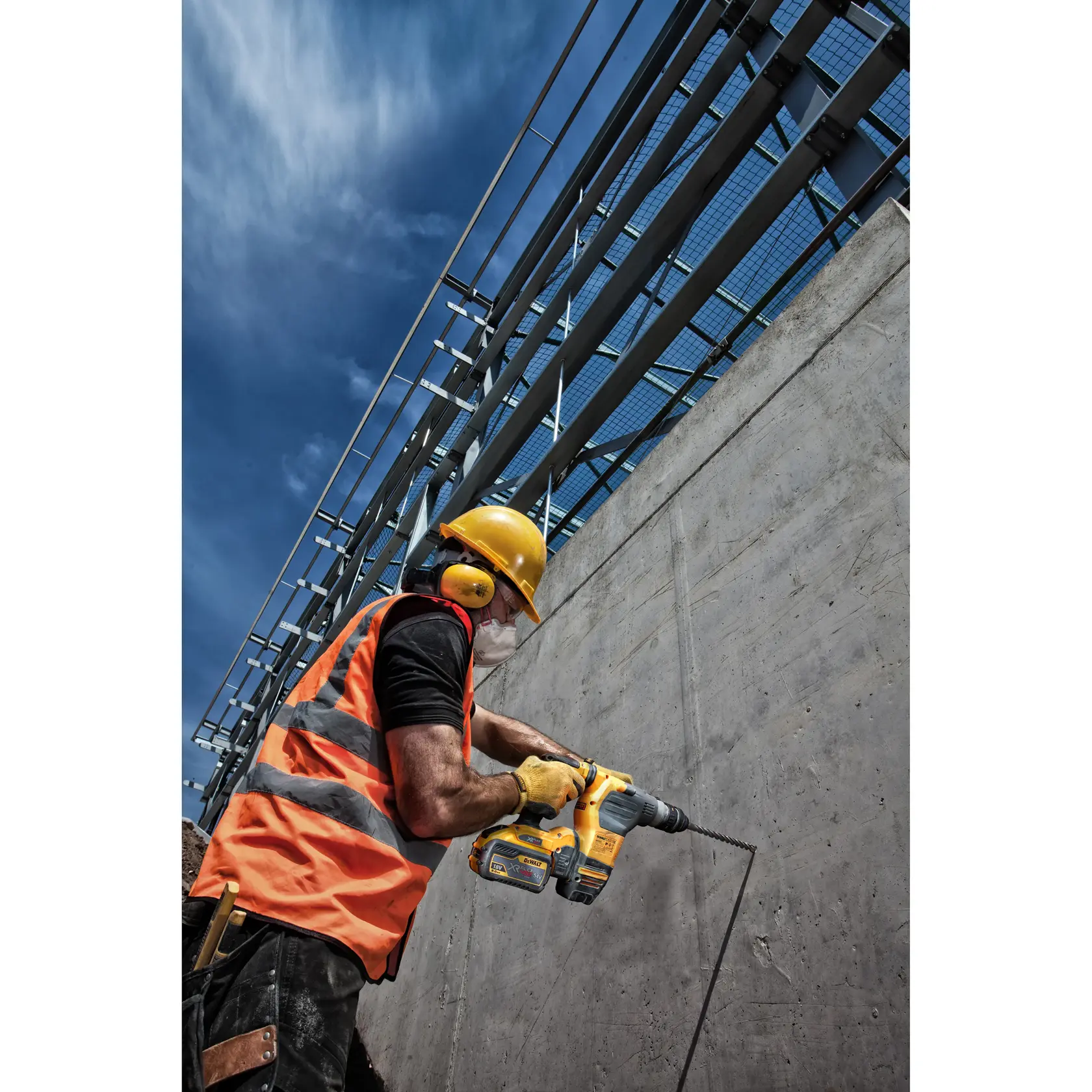 Trabajador con equipo de seguridad usa taladro DEWALT en una pared de concreto en construcción.