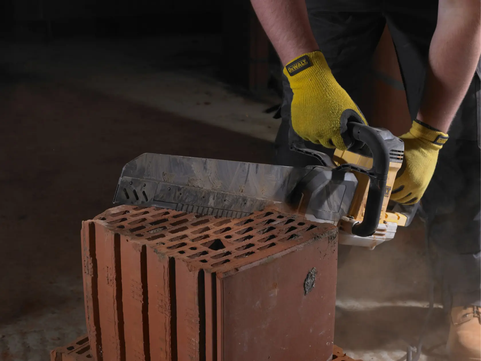 Person cuts a brick with a DEWALT power saw, wearing yellow gloves, in a construction setting.