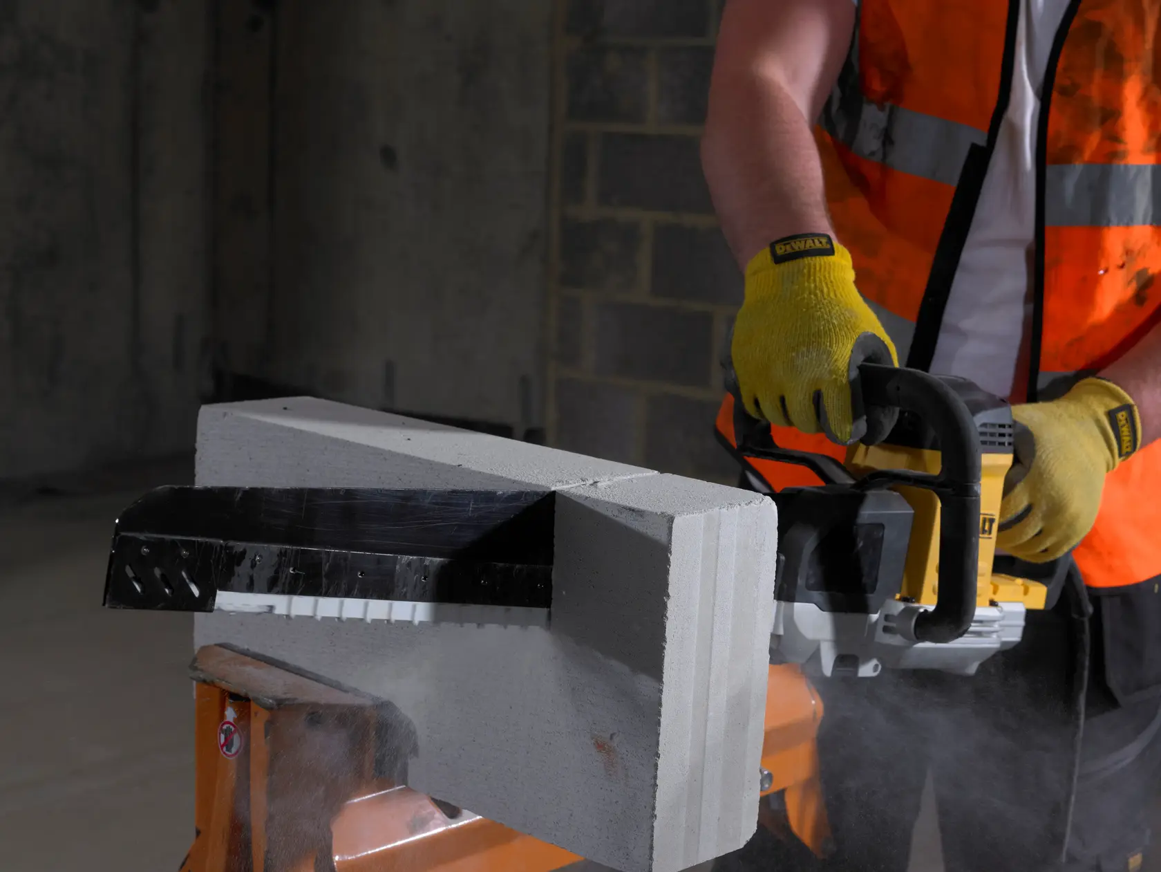 Worker cuts a concrete block with a DEWALT power saw, wearing gloves and safety vest, dust visible.