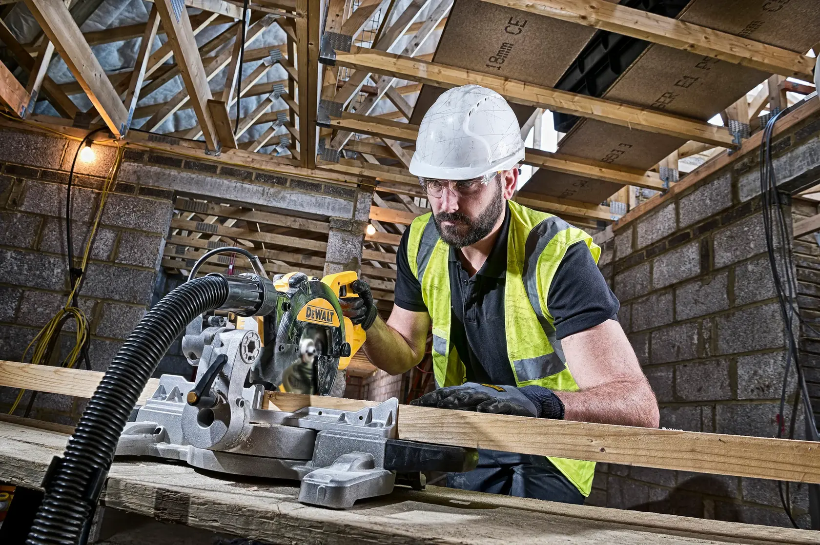 Photo of DEWALT DWS774 miter saw in use by worker cutting wood indoors at a construction site.
